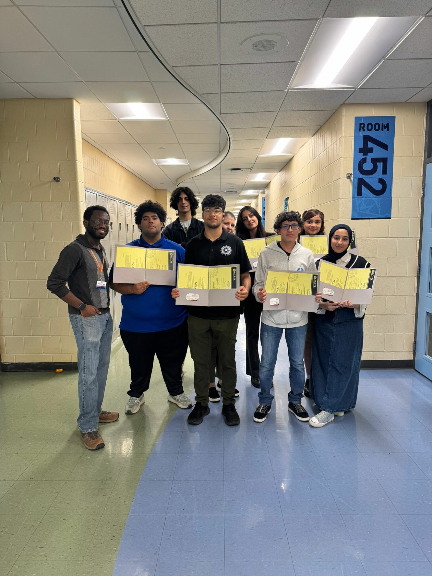 Group of seven people standing in hallway holding yellow boxes, with room 452 sign visible on wall.