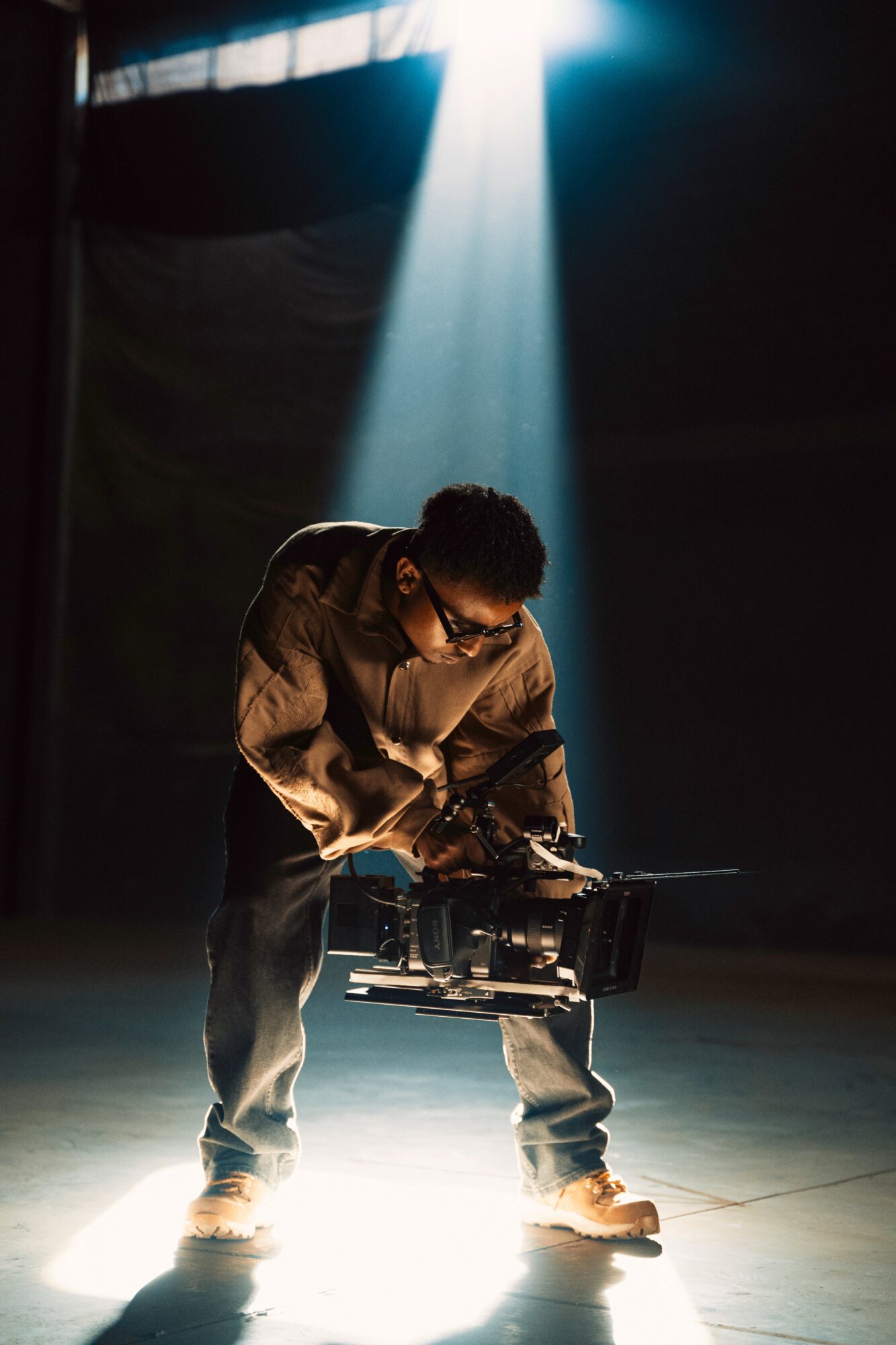Person operating a camera on a stage with a spotlight shining down from above.