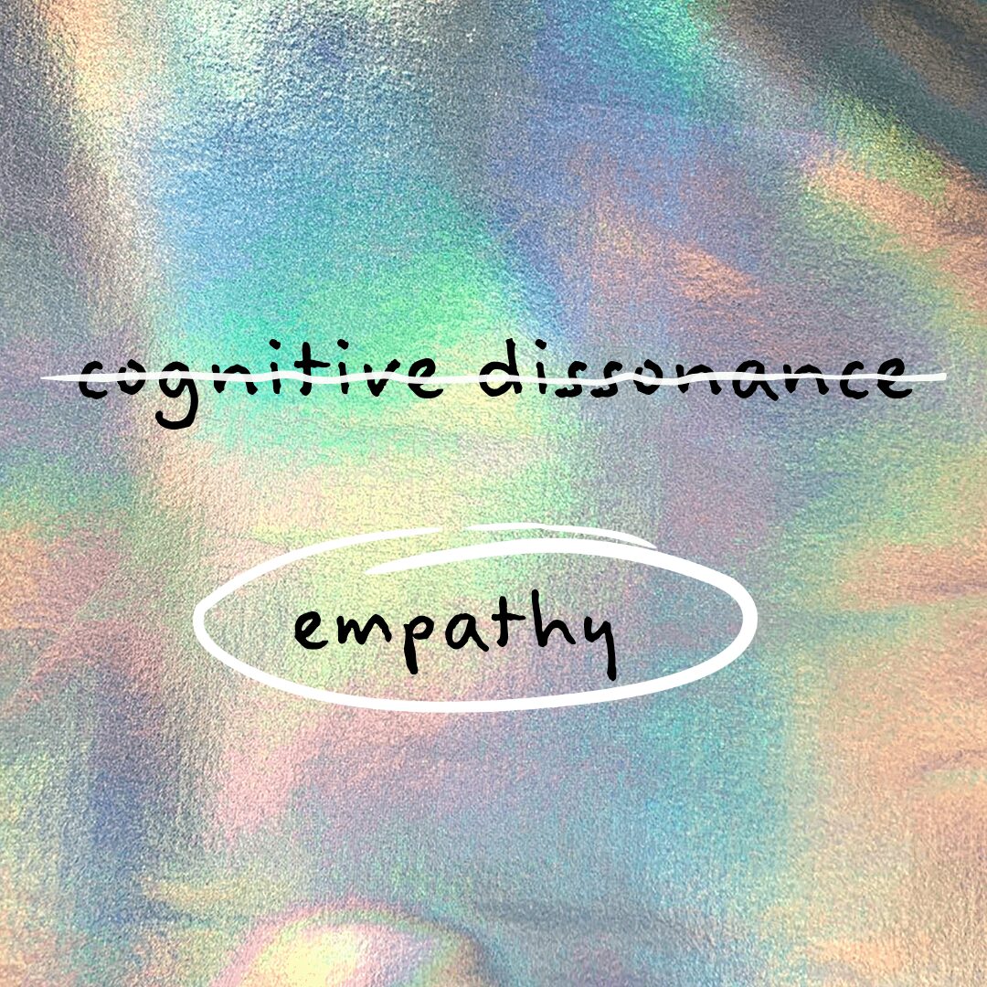 Colorful iridescent background with handwritten text 'cognitive dissonance' crossed out and 'empathy' circled.