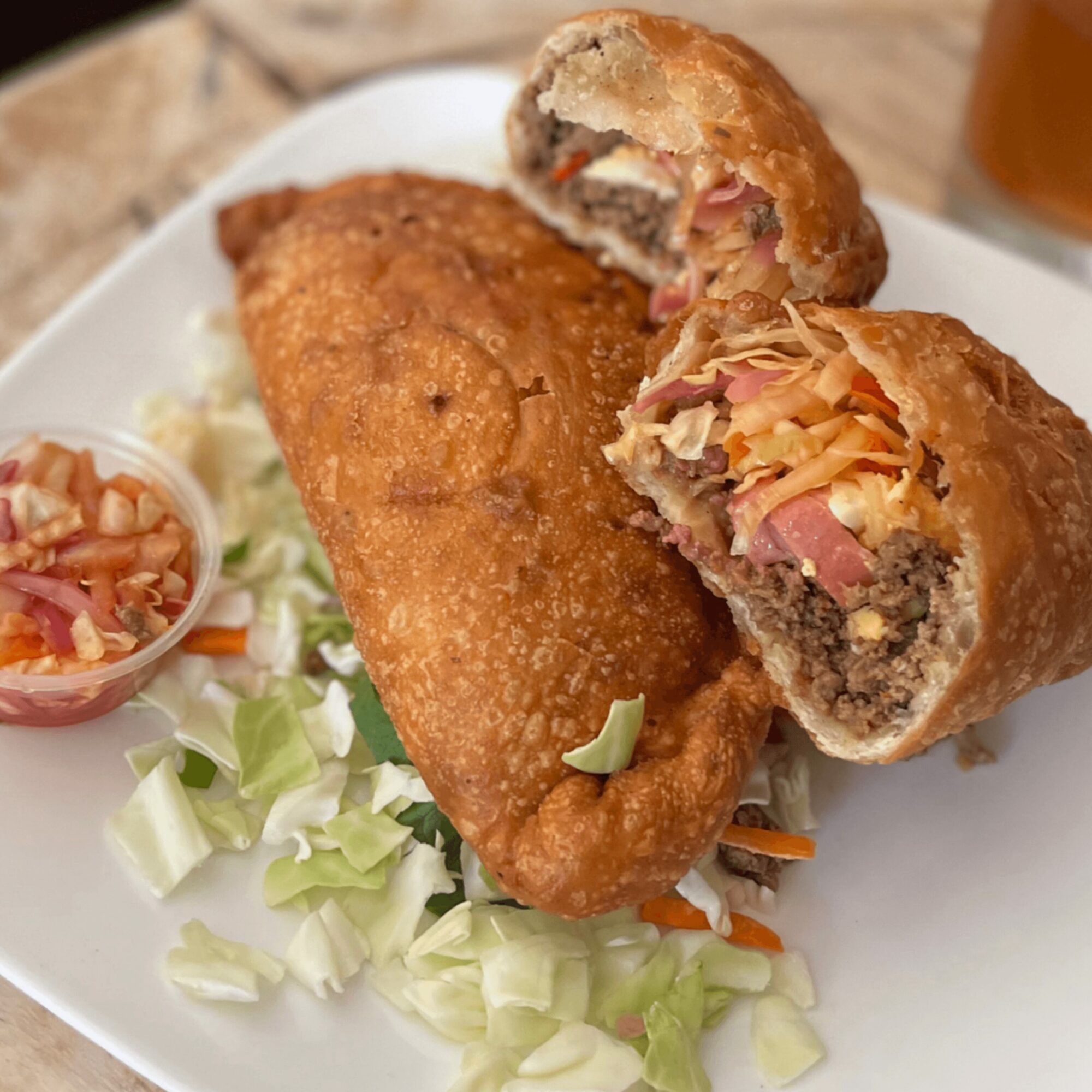 Two fried spring rolls, one cut open showing meat and vegetables, on a white plate with shredded lettuce and a small side of coleslaw.