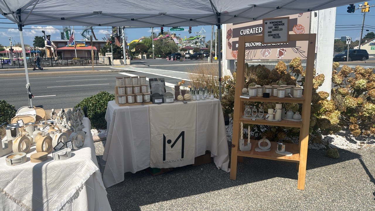 Outdoor market stall with candles and jars under a canopy, with a wooden shelf displaying more candles and jars.