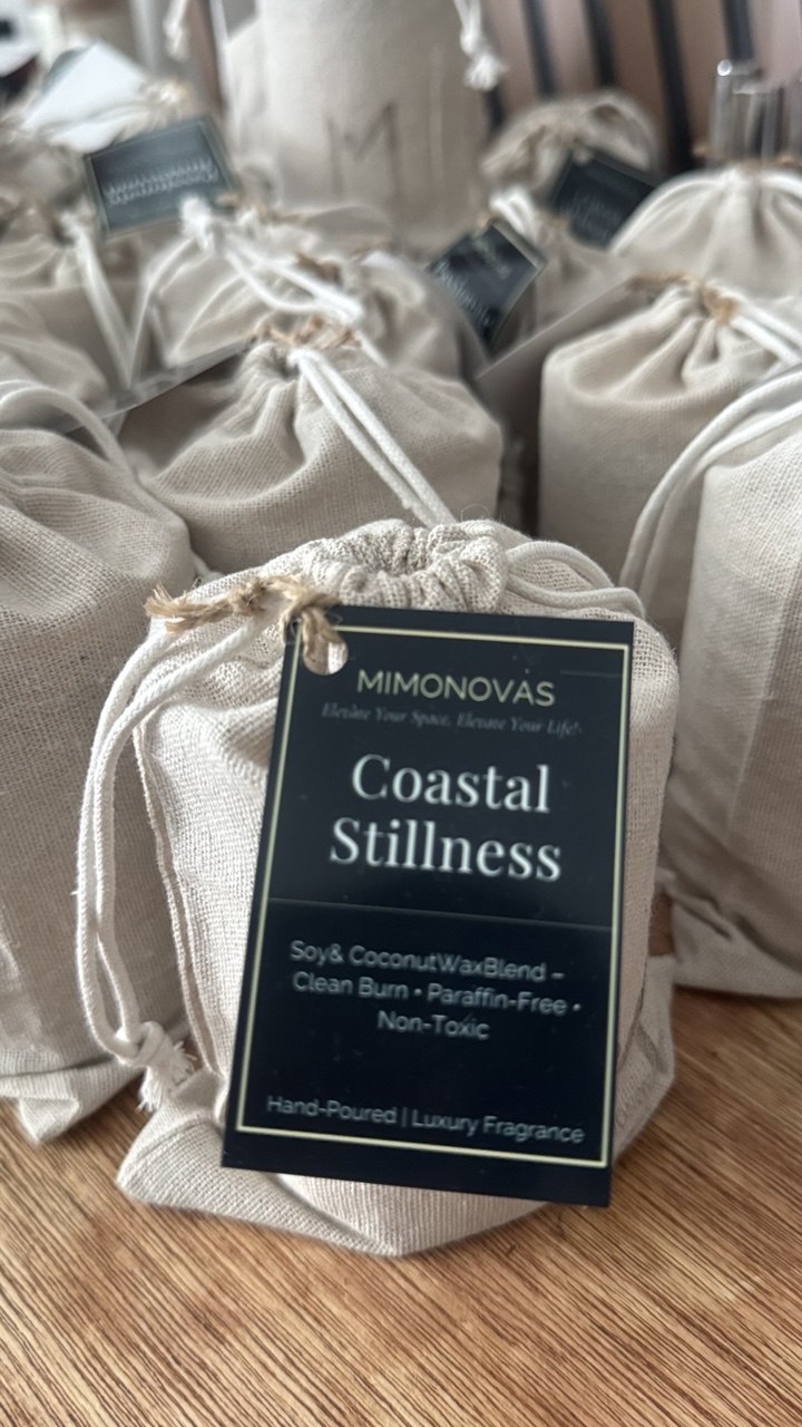 Multiple beige fabric pouches with a tag reading 'Coastal Stillness' on a wooden surface.
