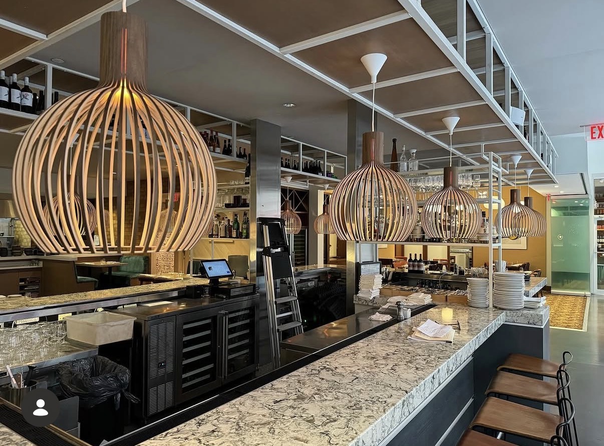 Bar counter with hanging wooden pendant lights, granite countertop, and shelves with bottles and glasses.