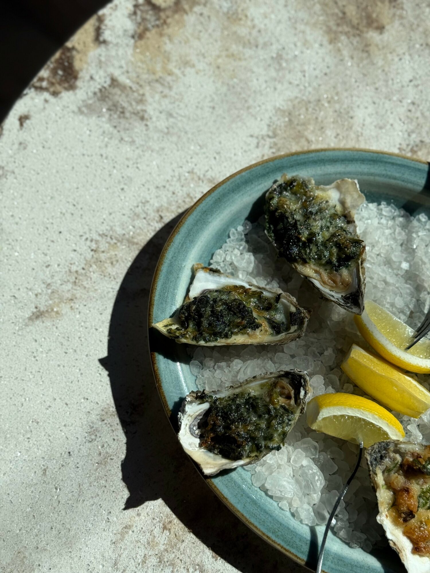 Seafood on ice with lemon wedges in a blue bowl, sunlight casting shadows, textured surface background.