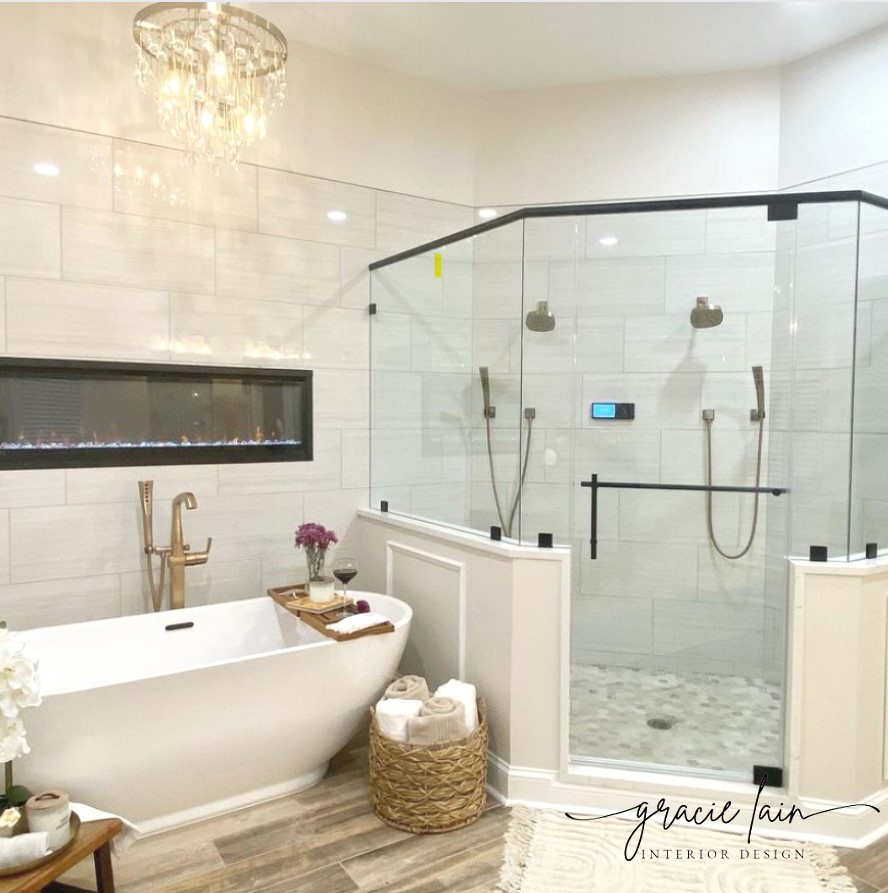 Bathroom with bathtub, glass shower enclosure, chandelier, and wooden floor, decorated with flowers and towels.