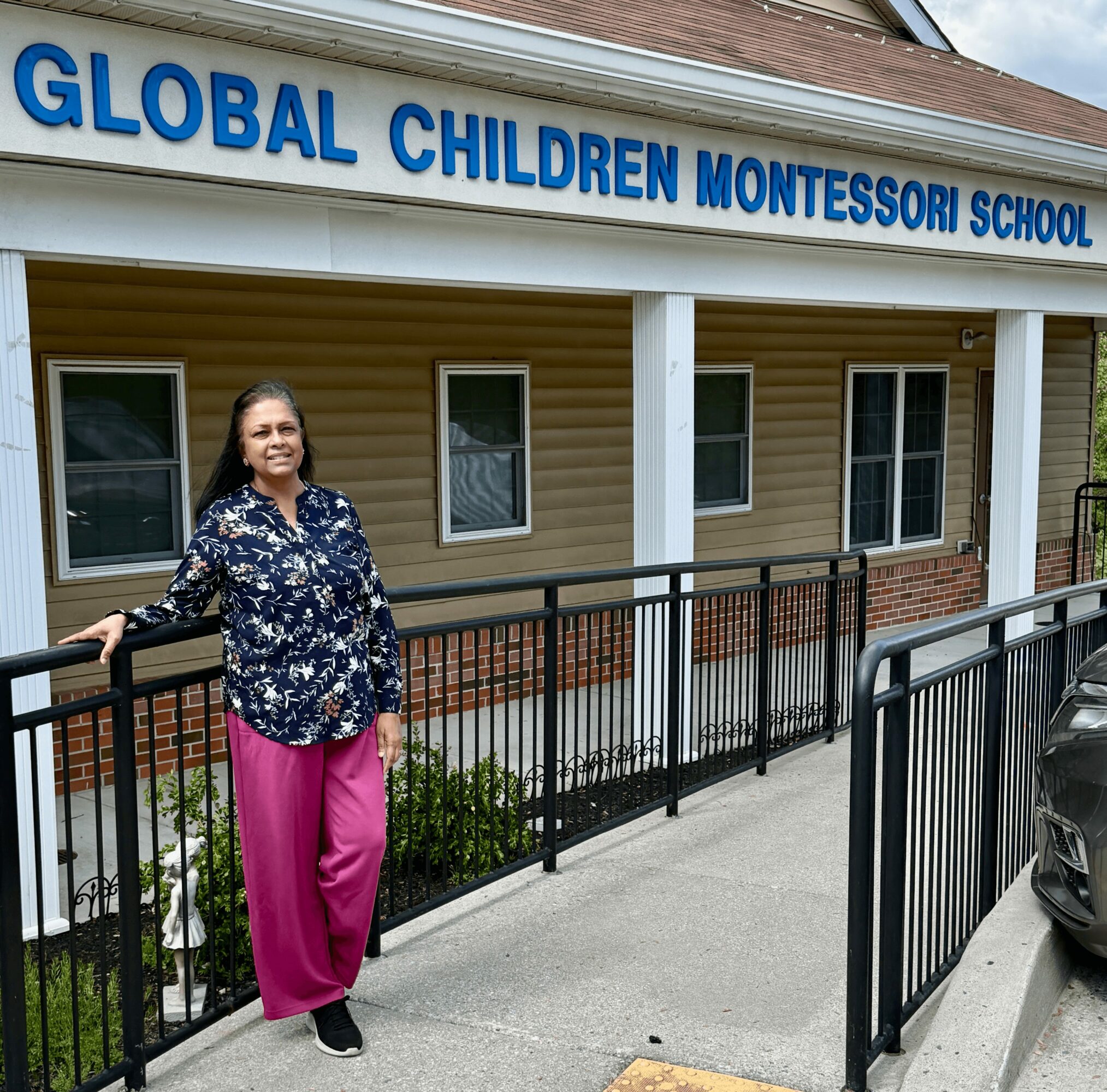 Woman standing outside a school building with a sign reading 'Global Children Montessori School'.
