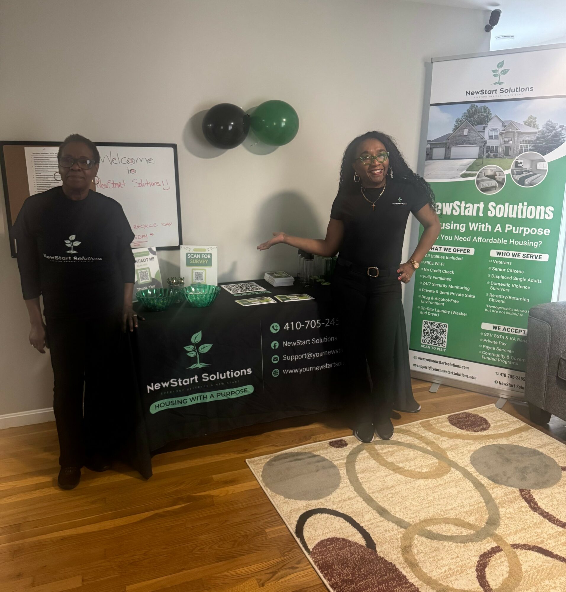 Two people standing next to a table with promotional materials, balloons on the wall, and a banner for NewStart Solutions.
