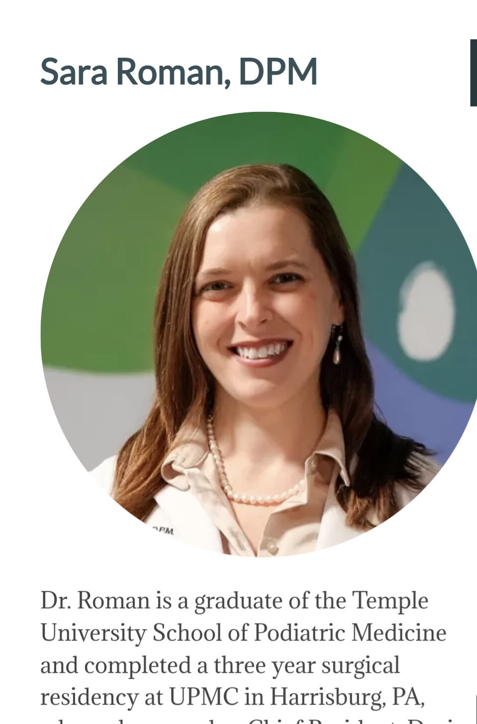 Portrait of a woman with brown hair smiling, wearing a white shirt and pearl necklace.