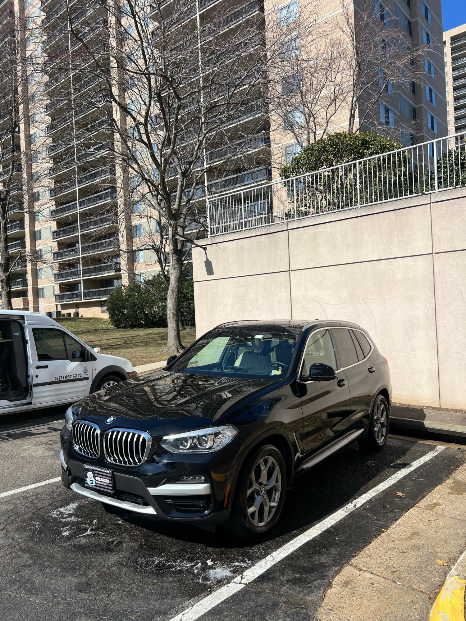 Black BMW SUV parked in a parking lot with buildings and trees in the background.
