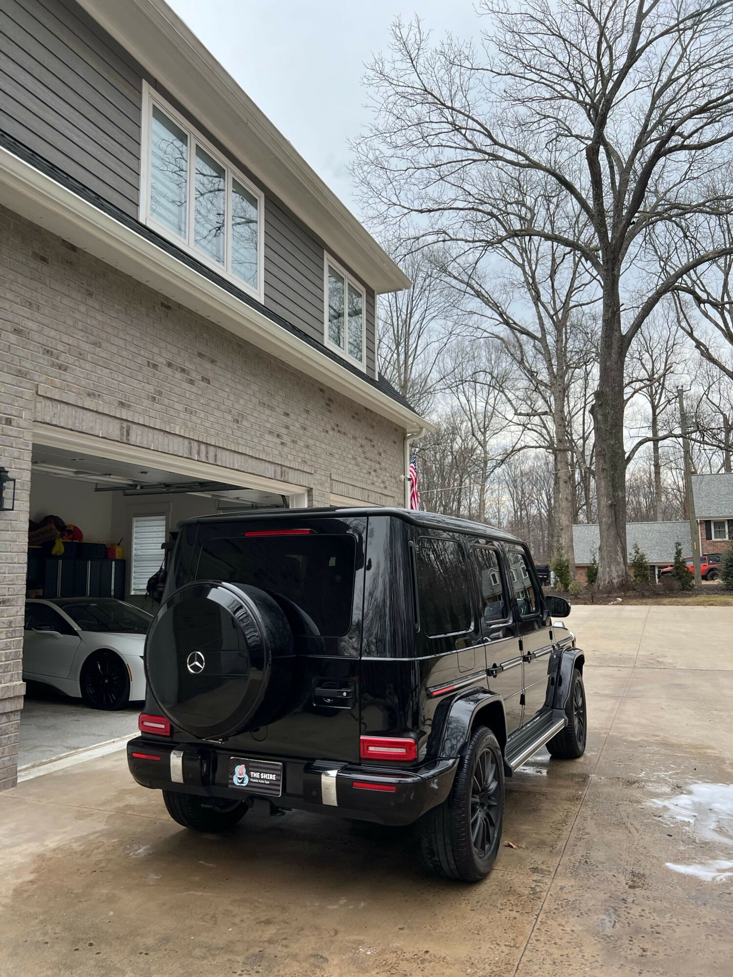 Black SUV parked outside a house with a garage, trees in the background, and a cloudy sky.