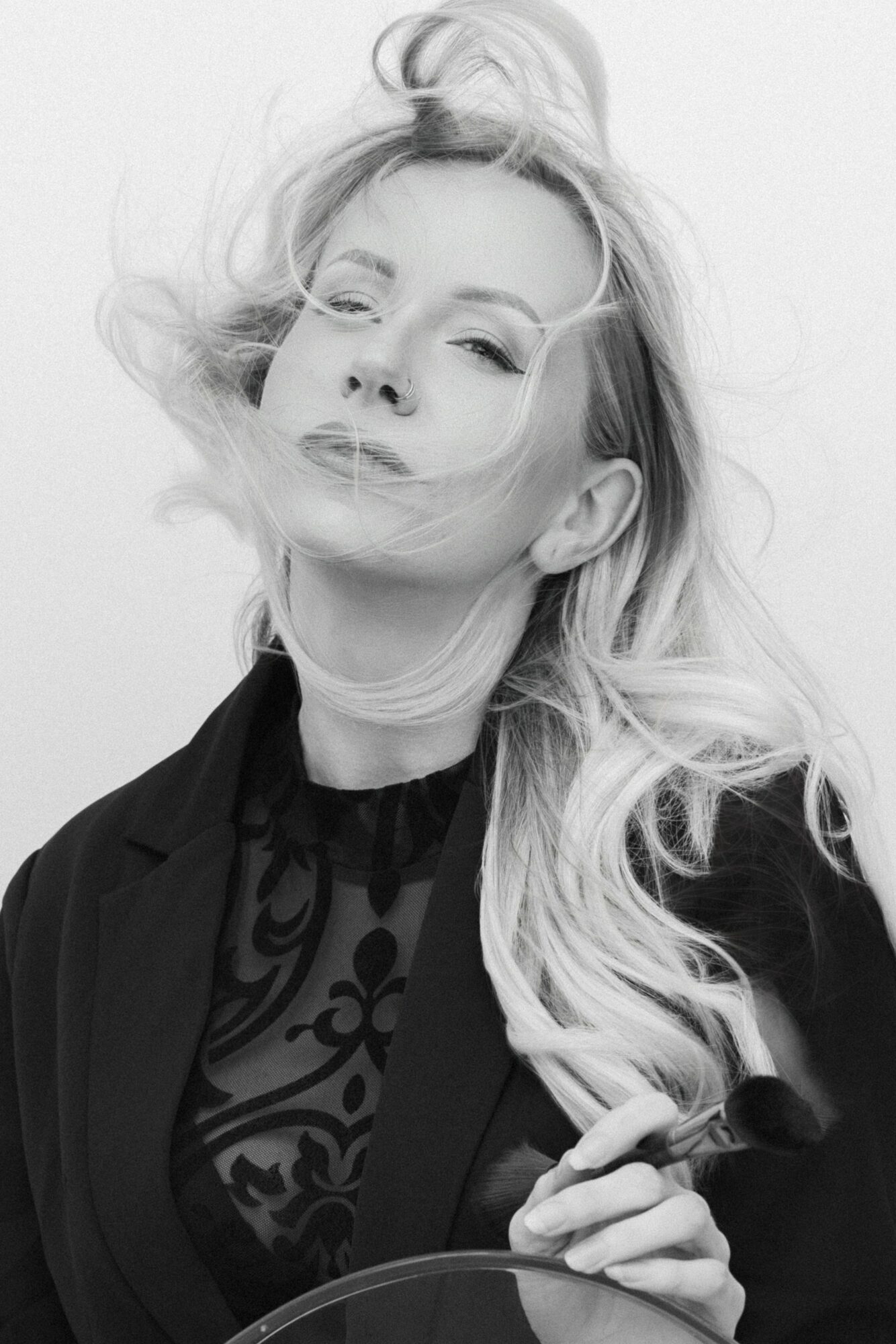 Woman with long, wavy hair and a confident expression, wearing a dark top and blazer.