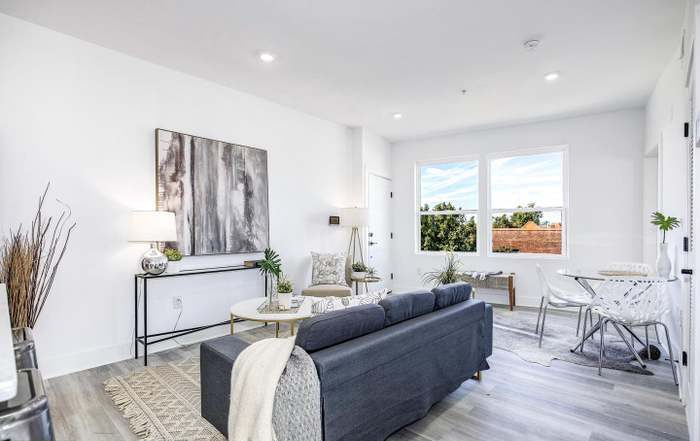Living room with a dark sofa, large windows, artwork, and minimal decor.
