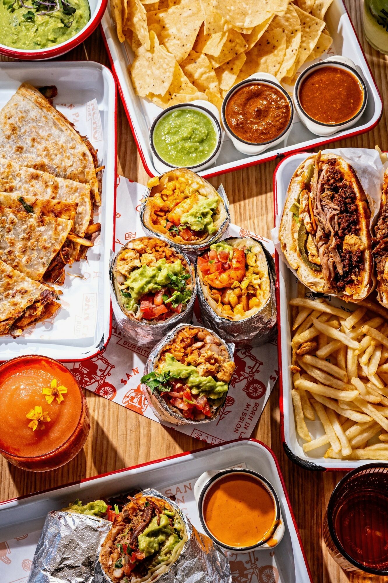 Assorted Mexican dishes including tacos, chips with salsa, guacamole, and beverages on a table.