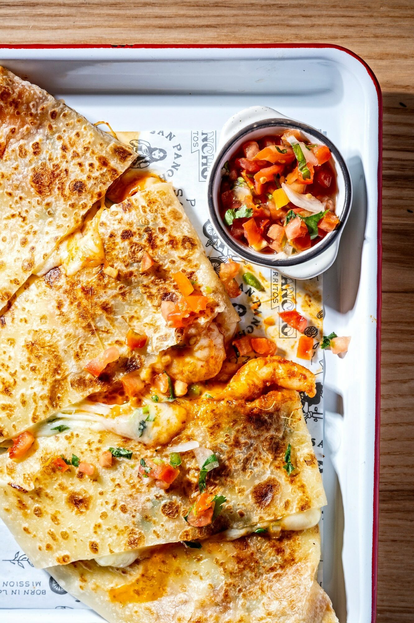 Three pieces of stuffed flatbread on a tray with a small bowl of tomato-based salsa.
