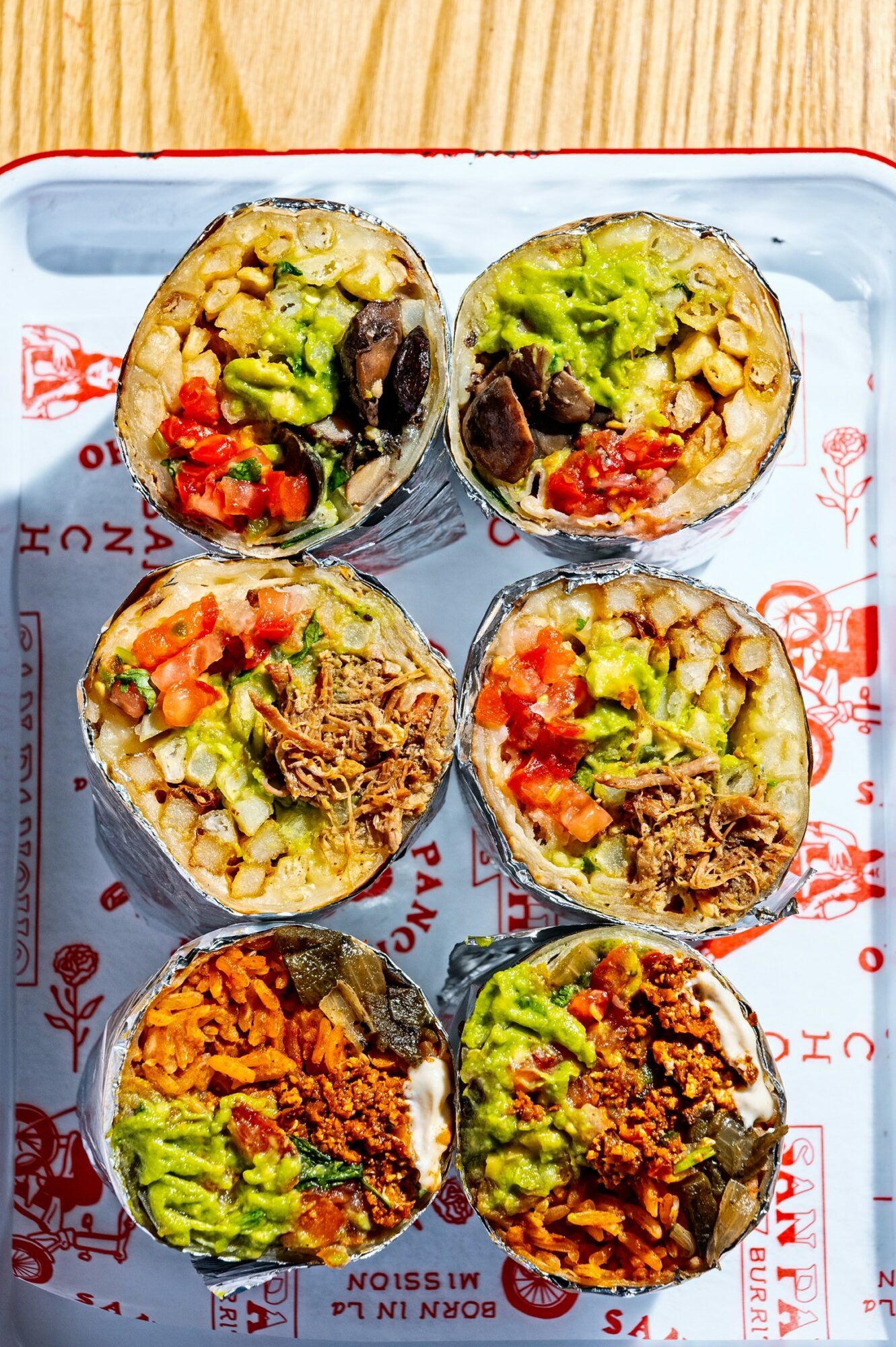 Six sushi rolls with rice, vegetables, and meat on a tray, arranged in two rows of three.