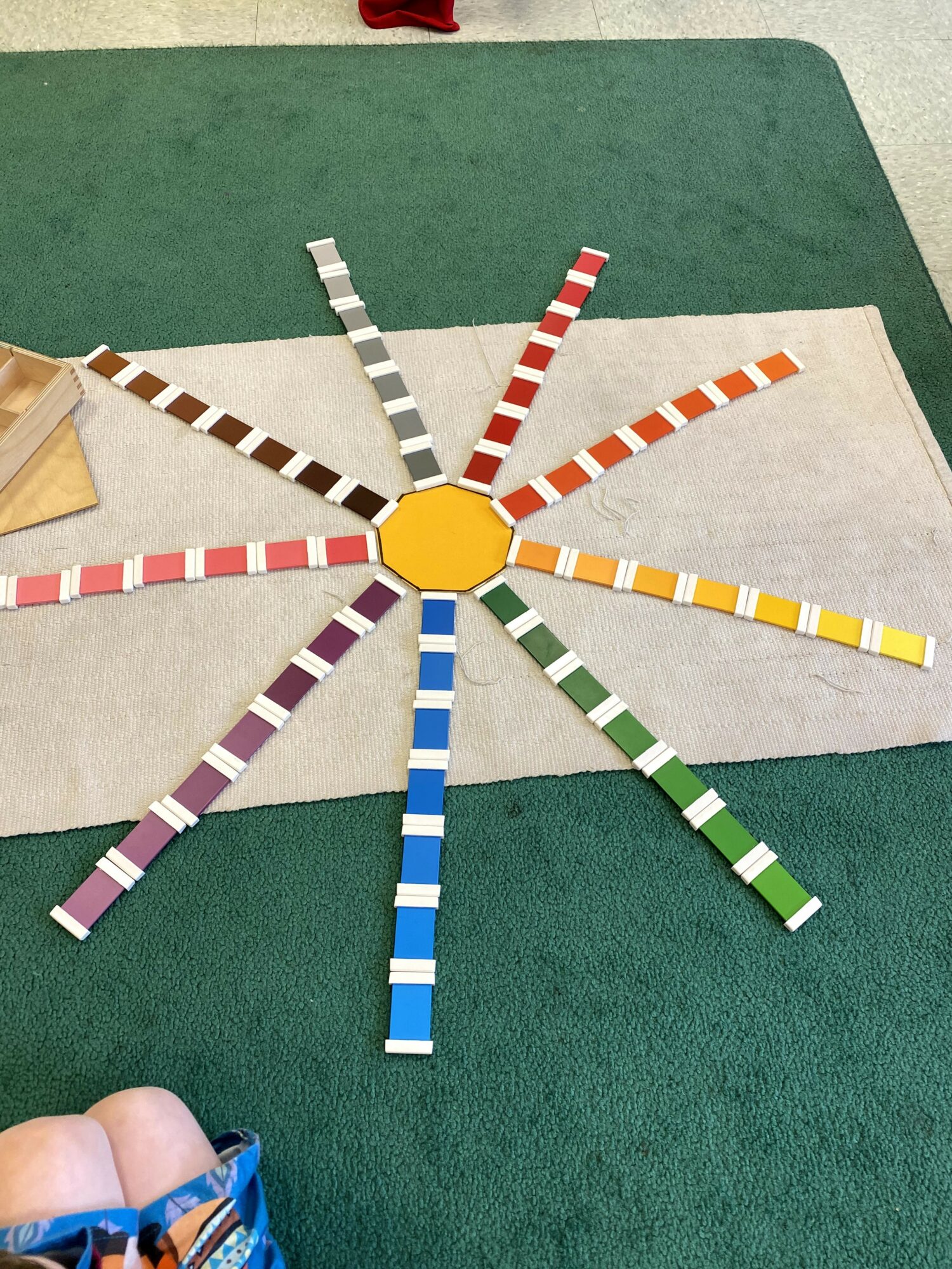 Colorful striped sticks arranged in a circle around a yellow hexagon on a green and white surface.