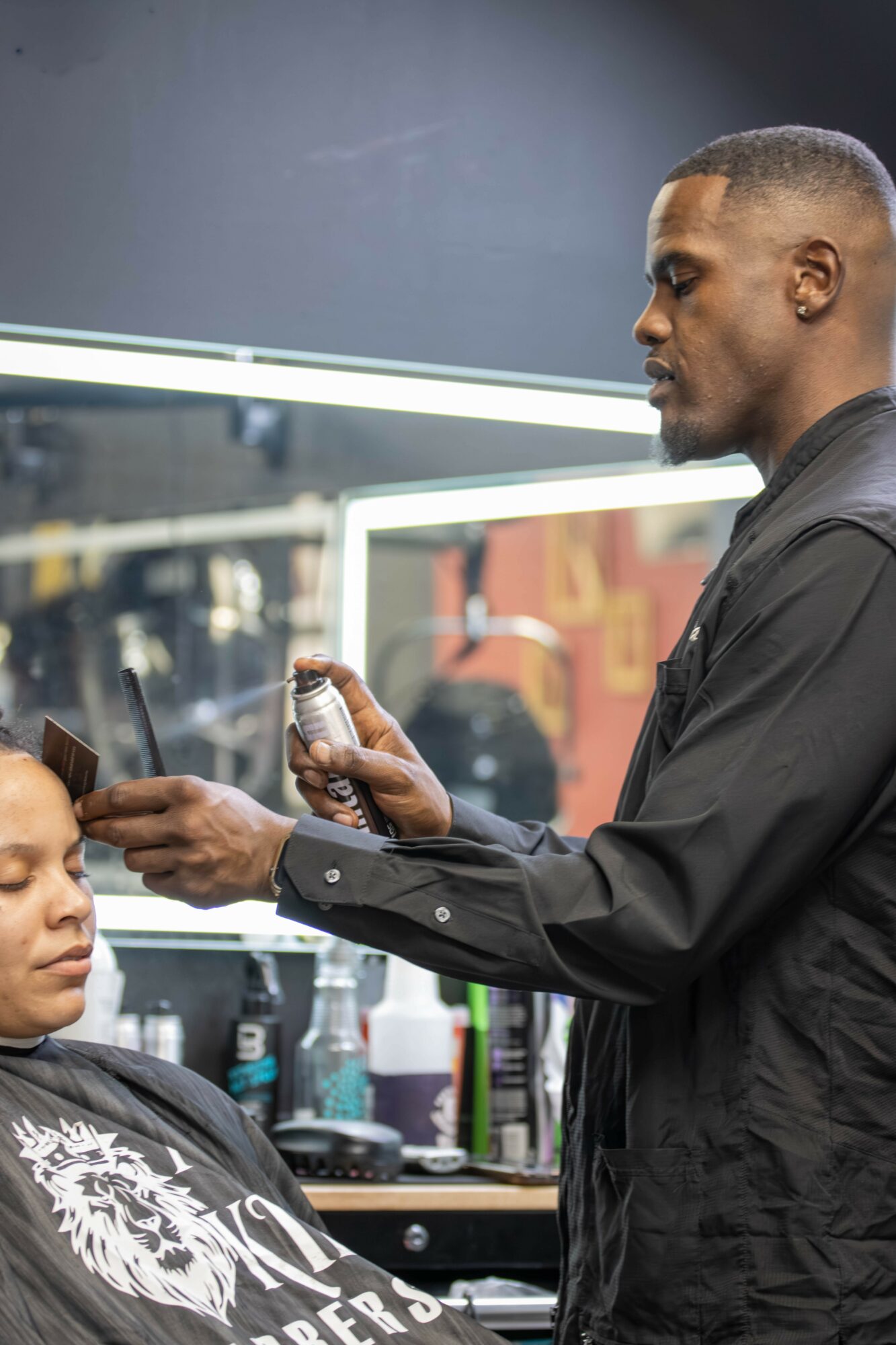 Barber holding a spray bottle and a comb, working on a client's hair in a salon.