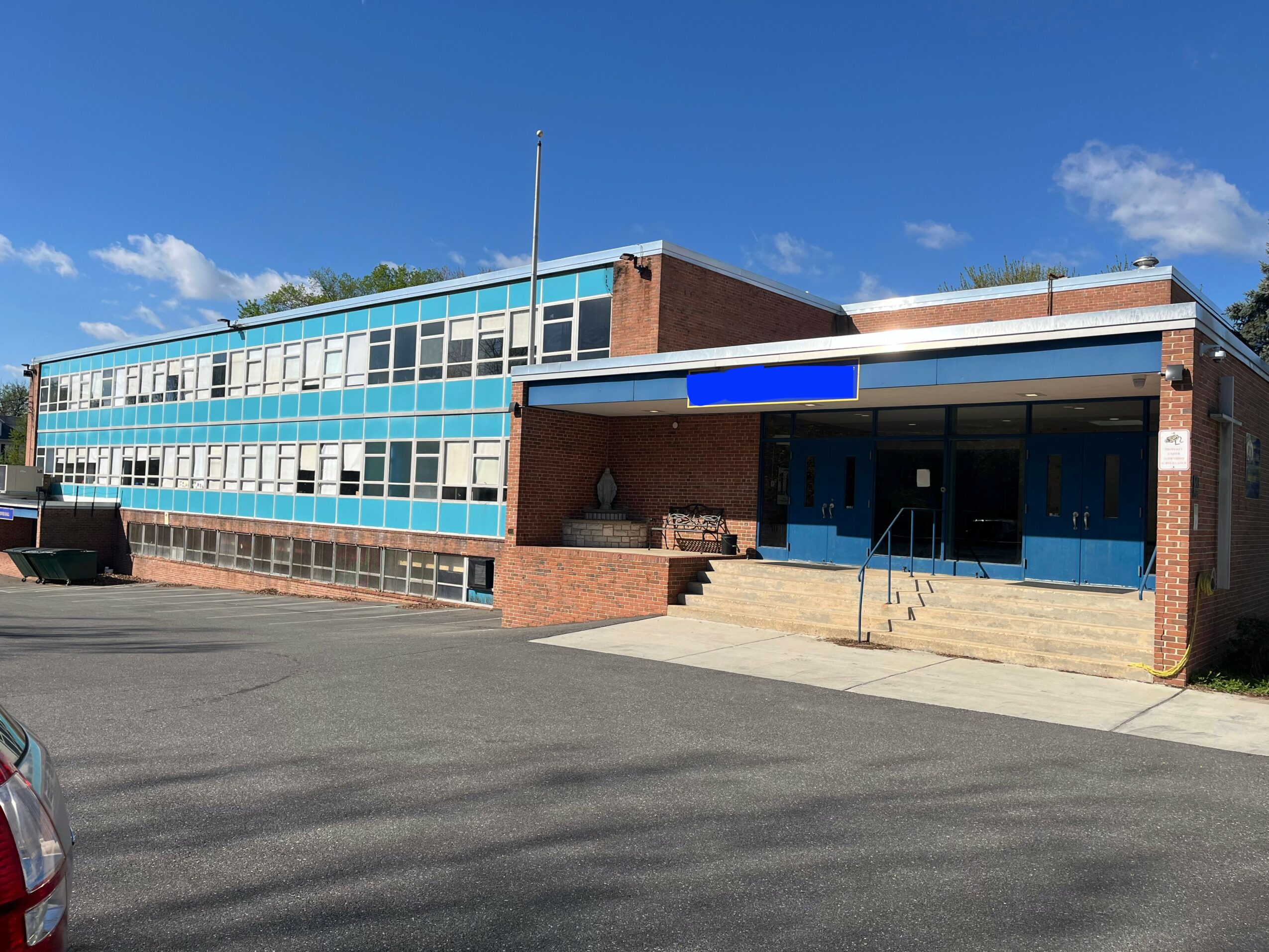 School building with blue and white exterior, brick entrance, and steps leading to doors under a blue sky.