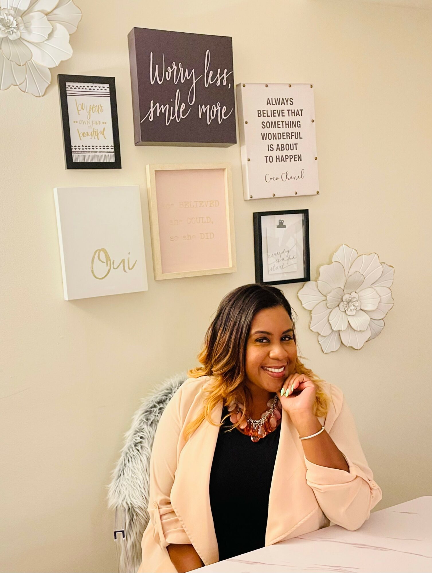 Woman sitting at a desk in front of a wall decorated with framed quotes and a large white flower wall art.