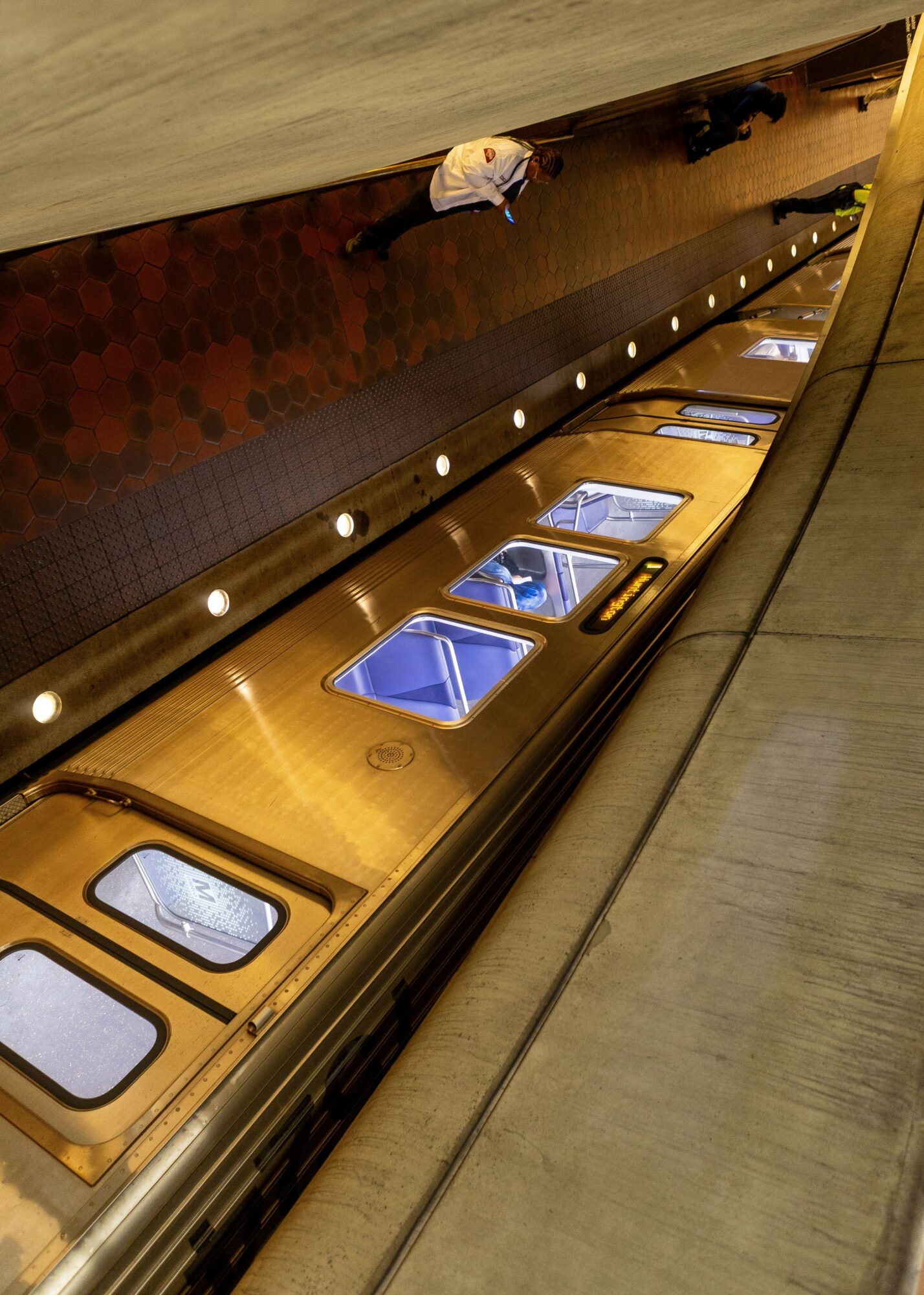 View of a long, curved conveyor belt with transparent containers and a person standing nearby.