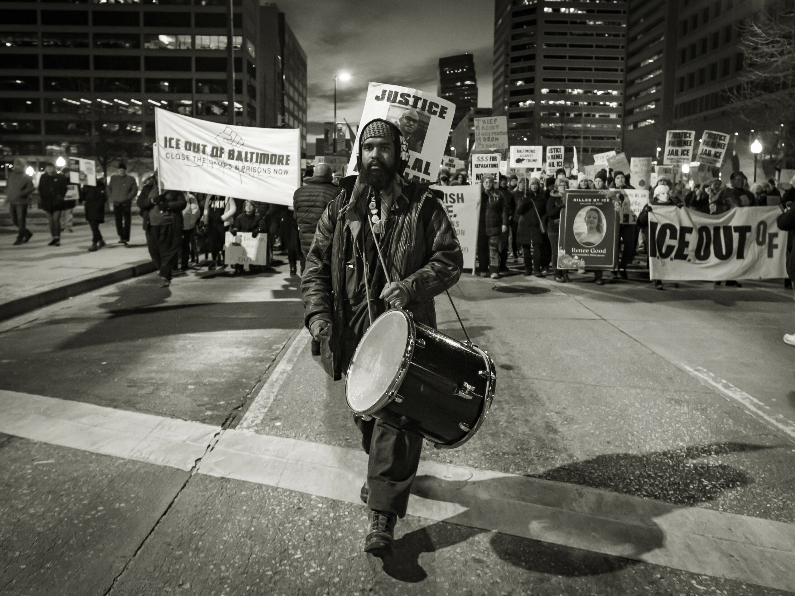 Person walking with drum in a protest march at night, holding a sign that says 'Justice'.
