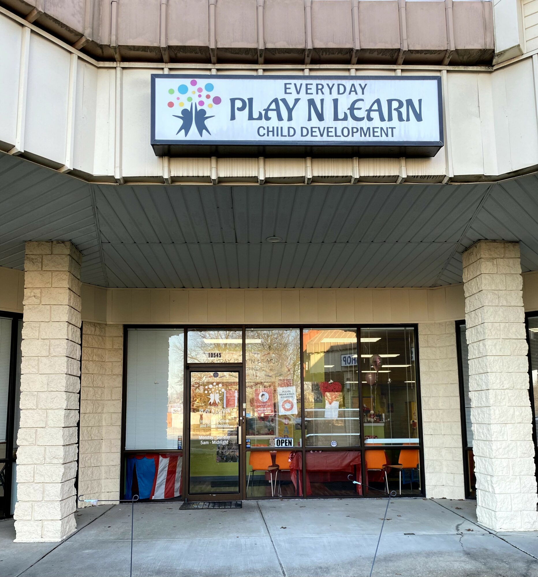 Building entrance with glass doors, brick columns, and a sign above reading 'Everyday Play & Learn Child Development'.