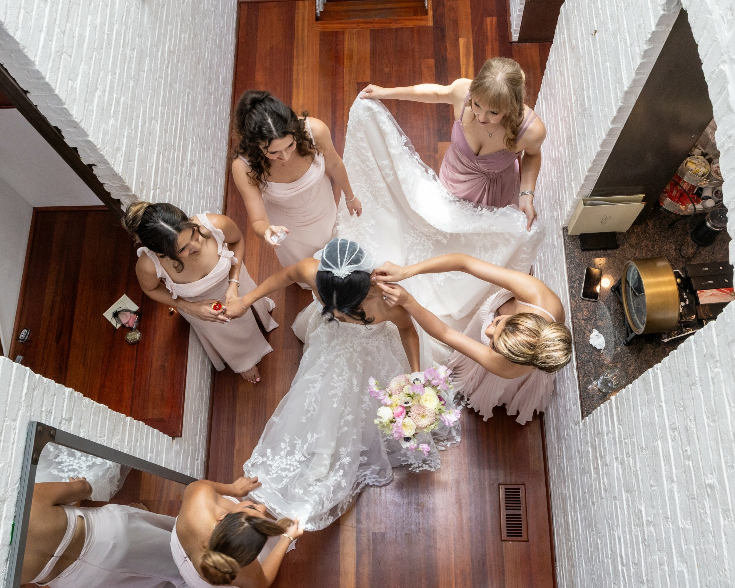 Six women, including a bride in a wedding dress, gather around in a hallway with wooden floors and white walls.