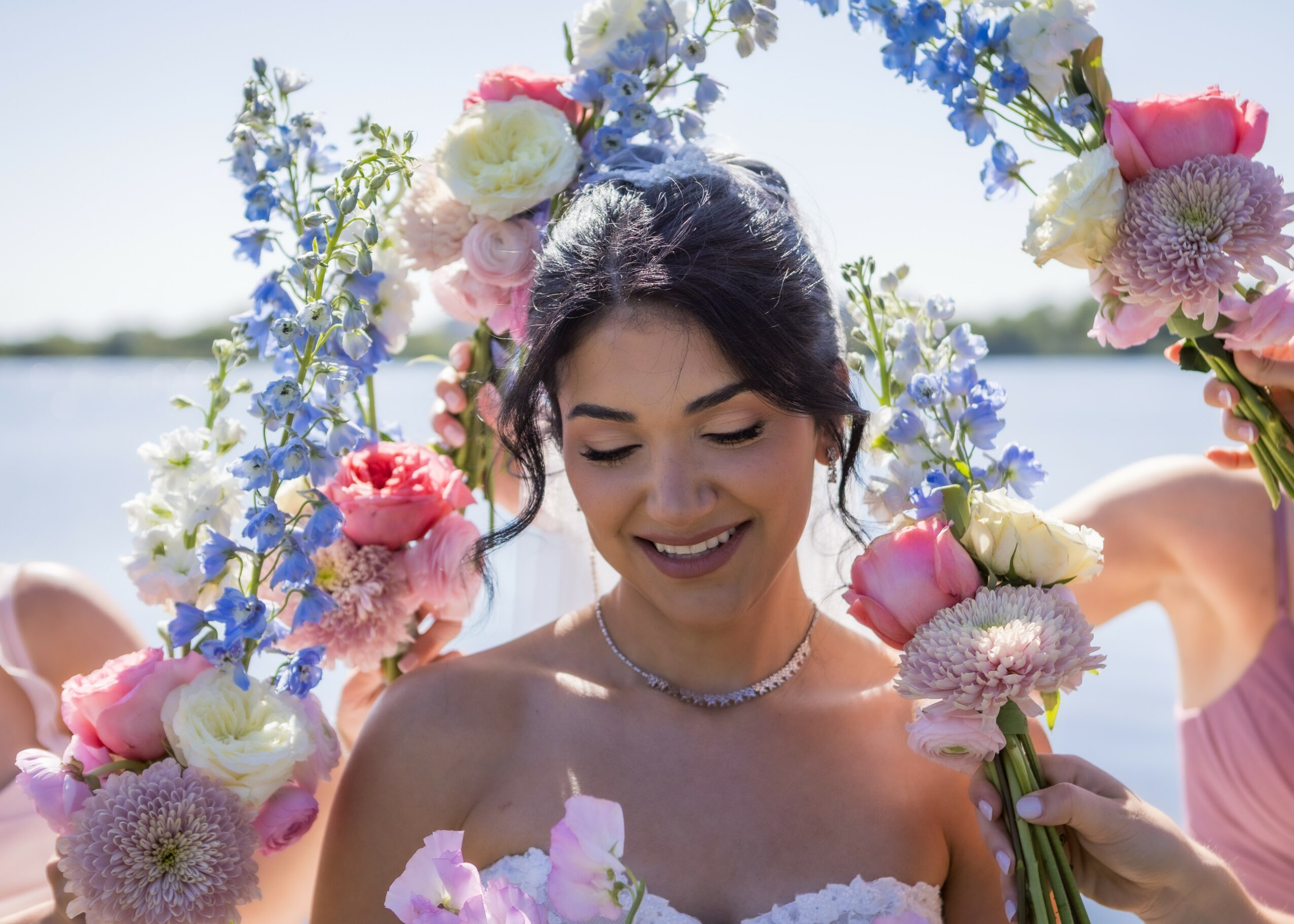Young woman with dark hair smiling, surrounded by colorful flowers in an outdoor setting.