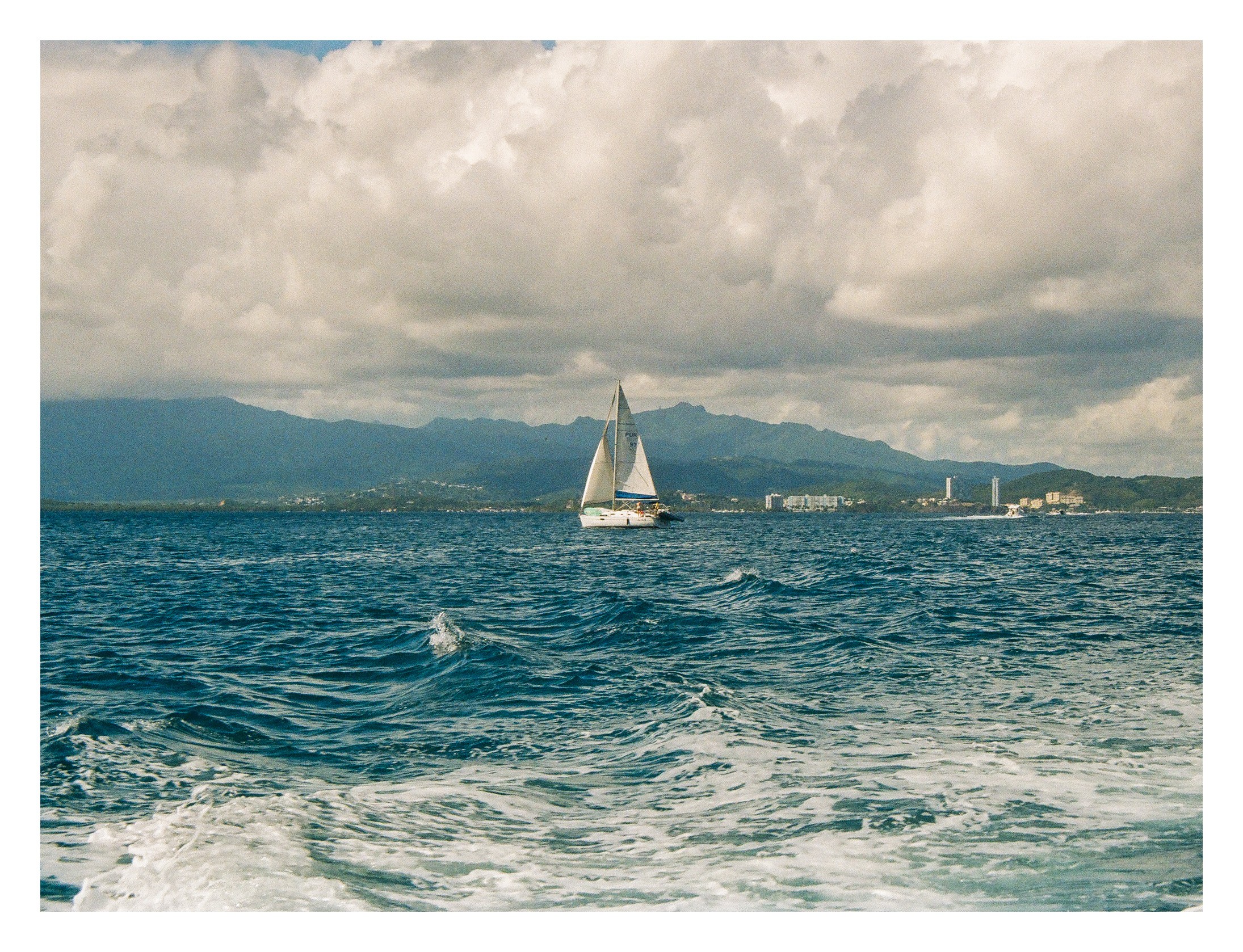 Sailboat on water with mountains and cloudy sky in background.