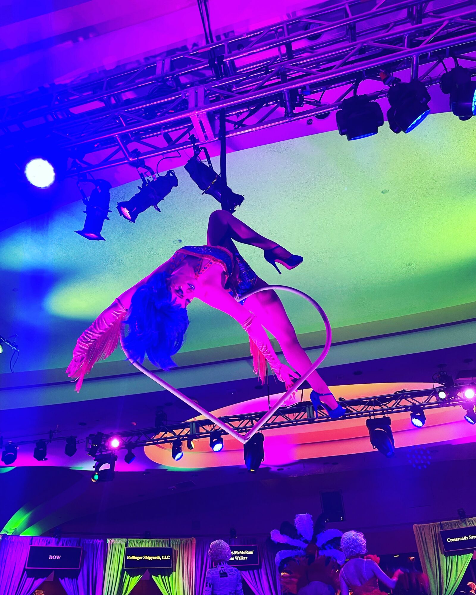 Two aerial performers hang upside down from hoops on stage with colorful lighting and a green backdrop.