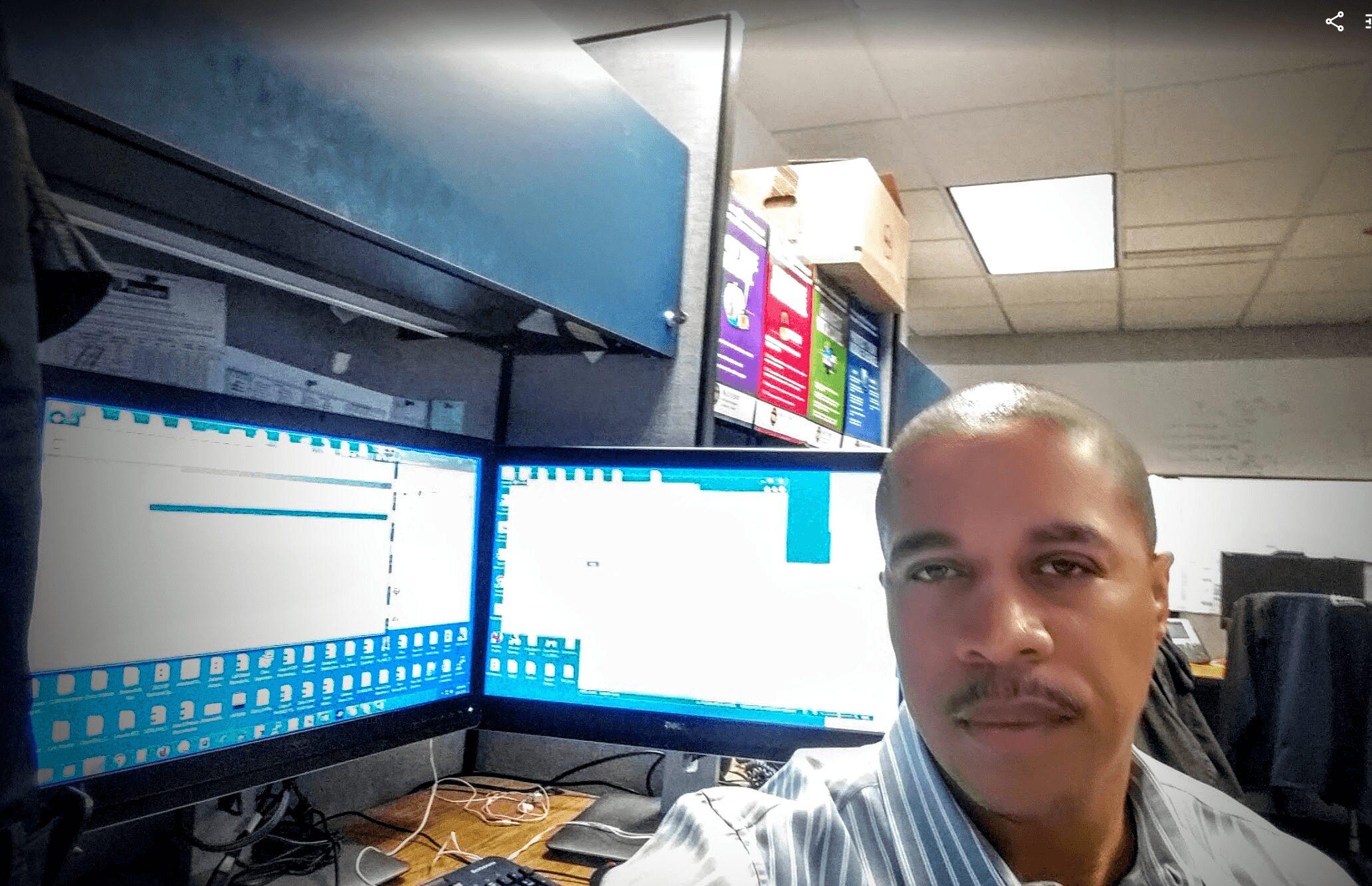 Man with short hair and mustache in an office with multiple computer monitors displaying charts and data.