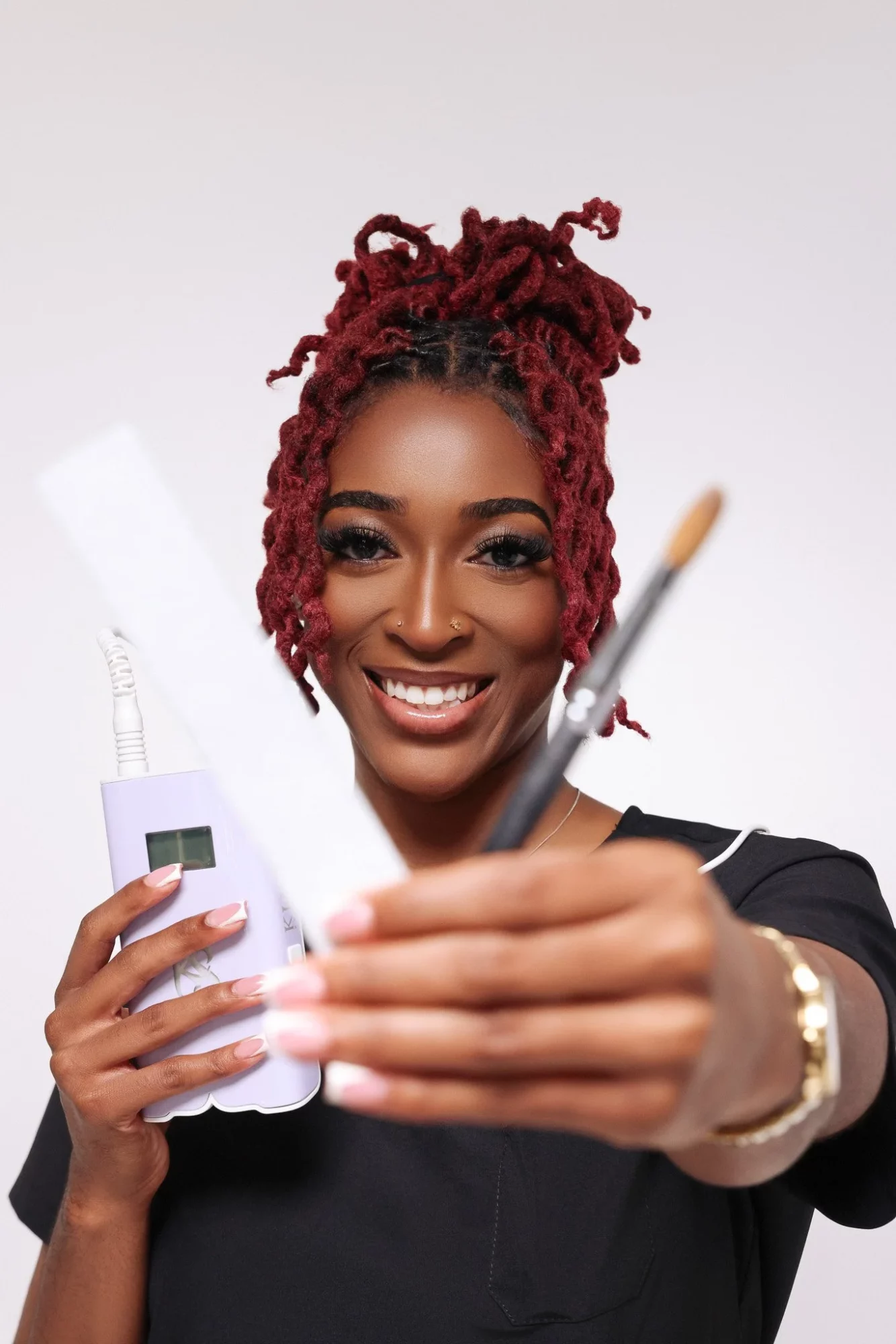Smiling woman with red dreadlocks holding a syringe and a small bottle, pointing it towards the camera.