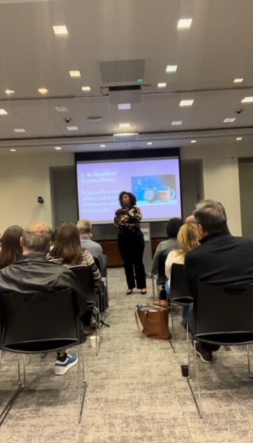 Person standing in front of a presentation screen addressing an audience in a conference room.