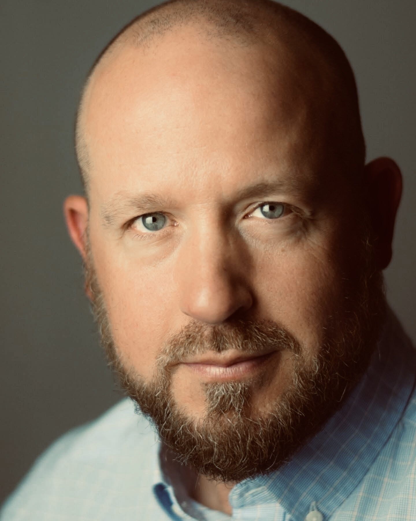 Close-up portrait of a man with a beard and blue eyes, wearing a light blue shirt.