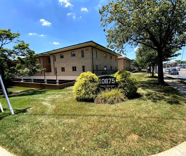 Building with brick exterior, surrounded by trees and grass, under a blue sky with clouds.