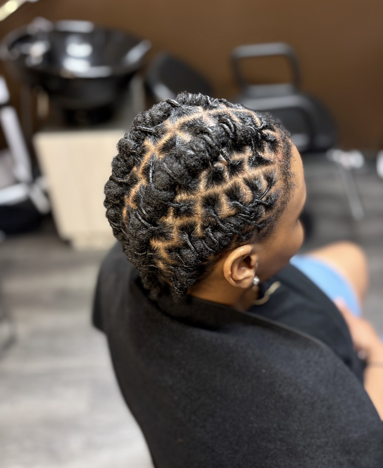 Person with braided hairstyle, viewed from above, sitting in a salon or barbershop.