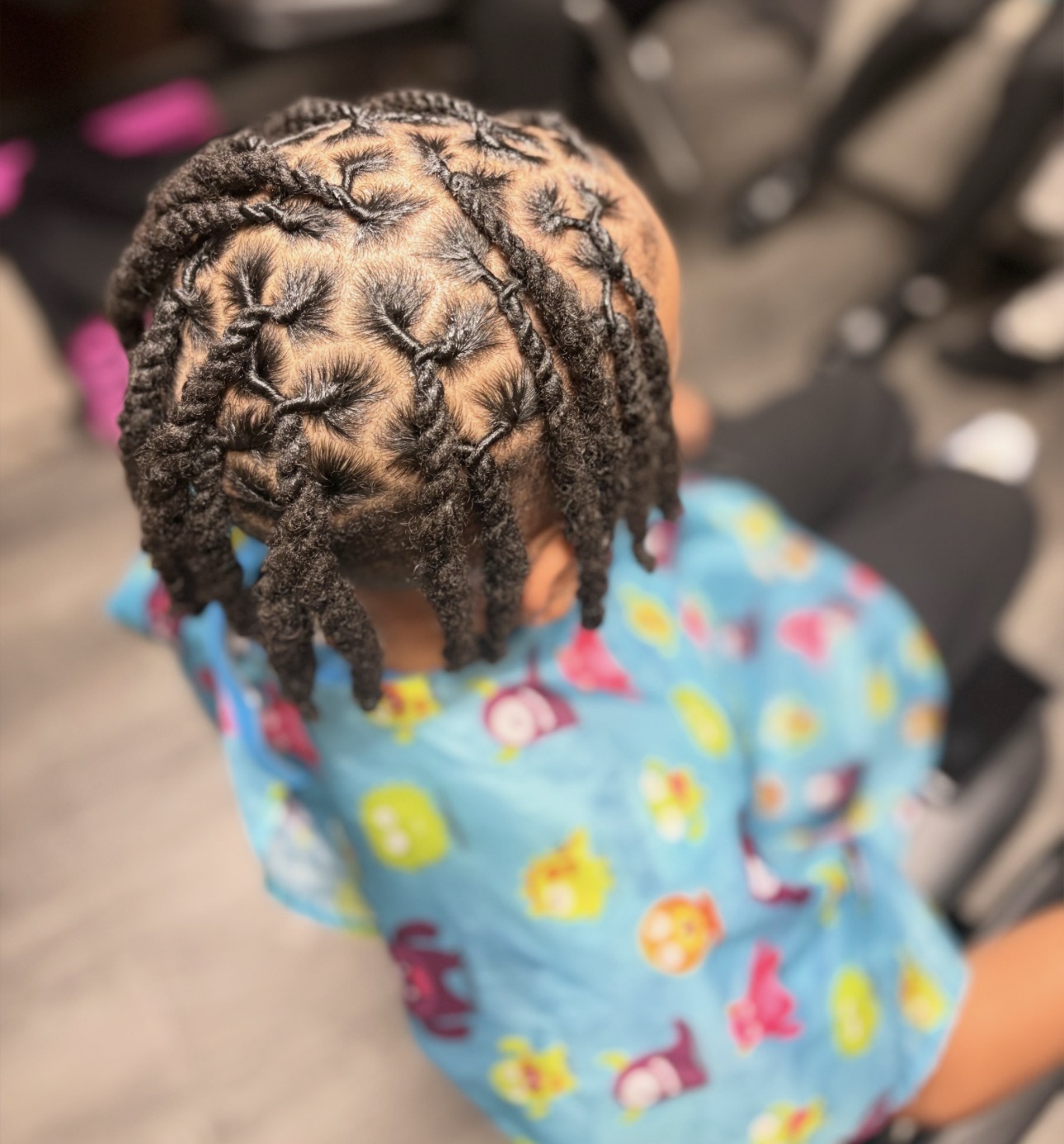 Child with braided hair wearing a colorful shirt, sitting indoors with blurred background.