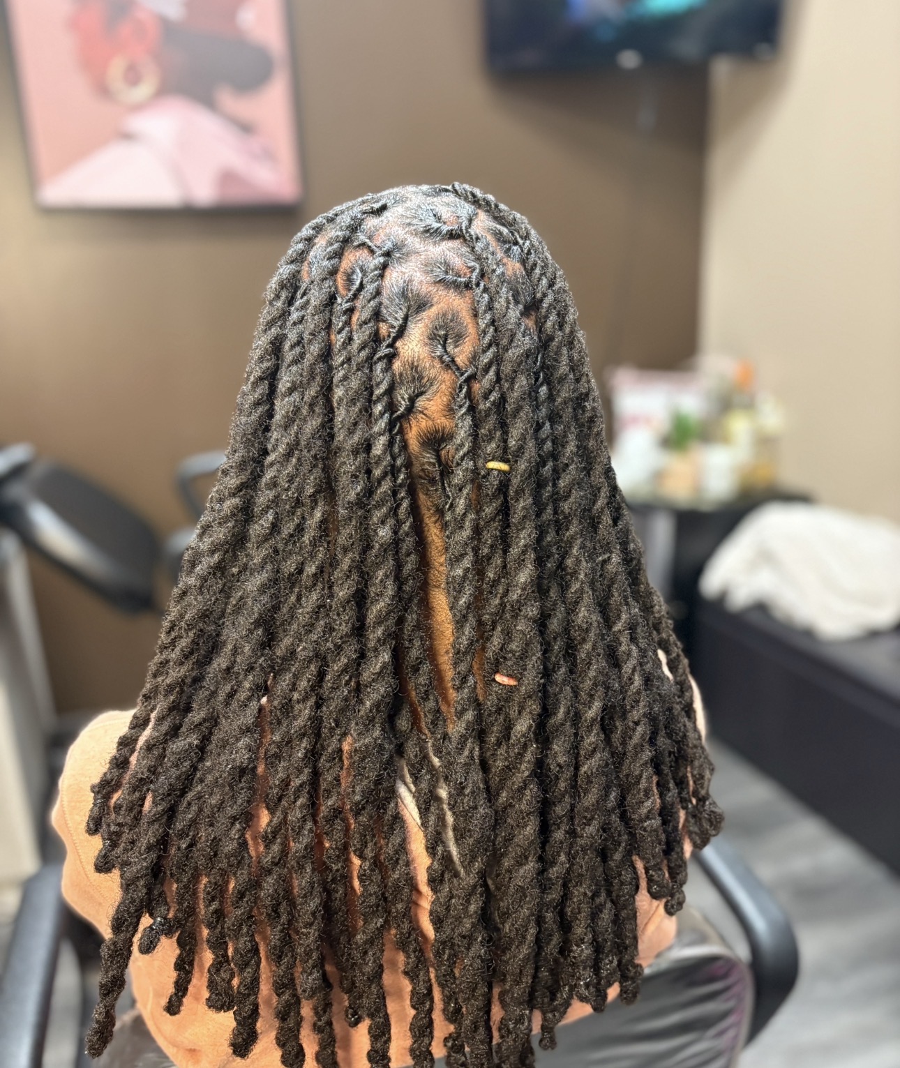 Person with long, thick dreadlocks facing away, in a room with a television and framed picture on the wall.