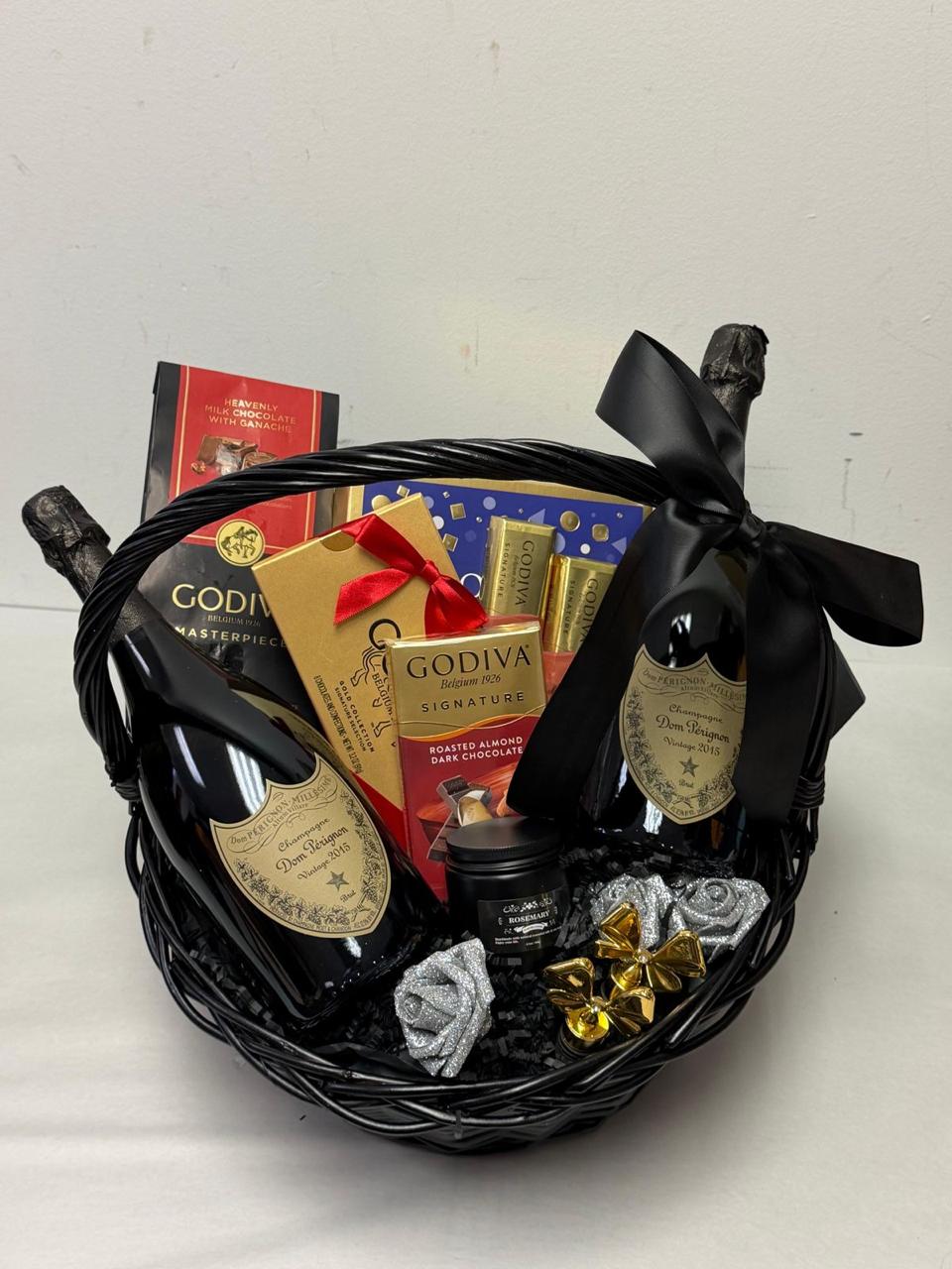 Black gift basket with chocolates, gold and red ribbons, and a black bow, placed against a plain background.