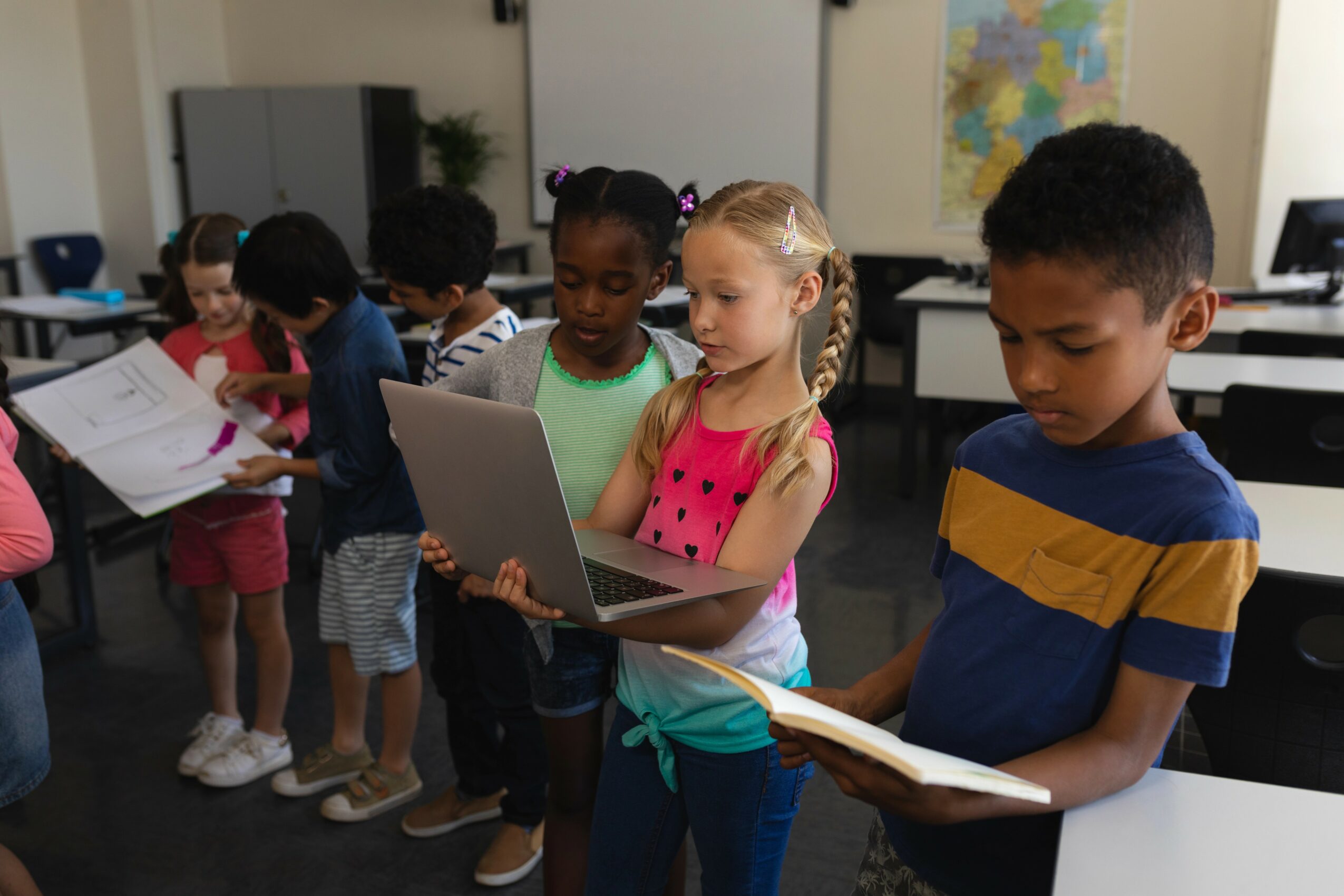 Group of children in classroom using laptops and books, engaging with learning activities.