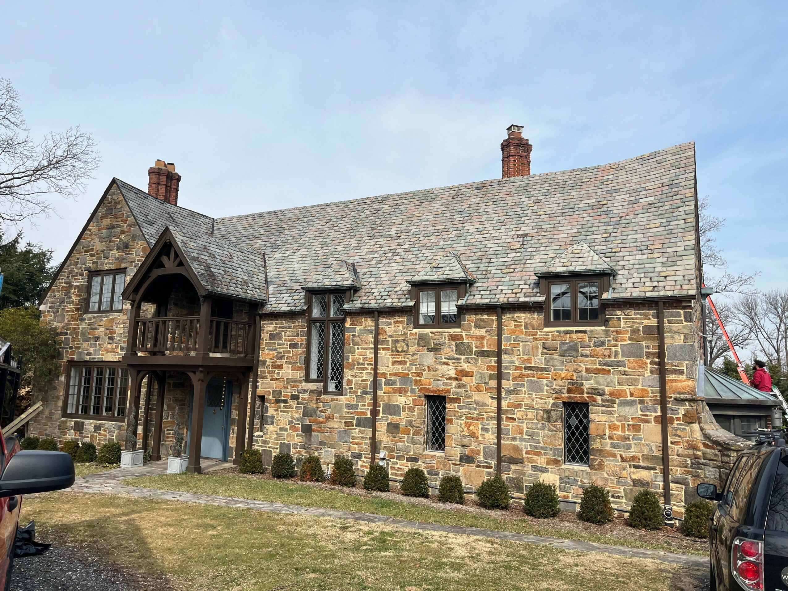 Stone house with steep roof, small windows, and a front porch, surrounded by a lawn and small bushes.