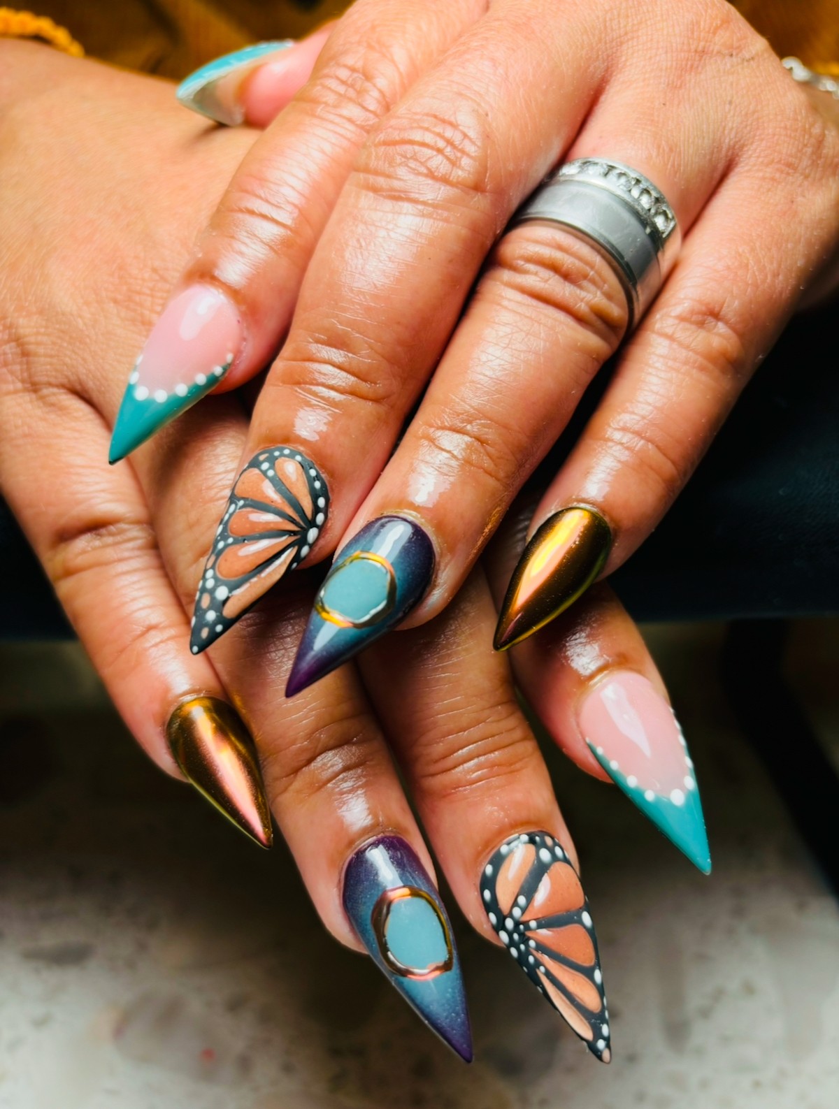 Close-up of hands with colorful, decorated nails and a silver ring on the middle finger.