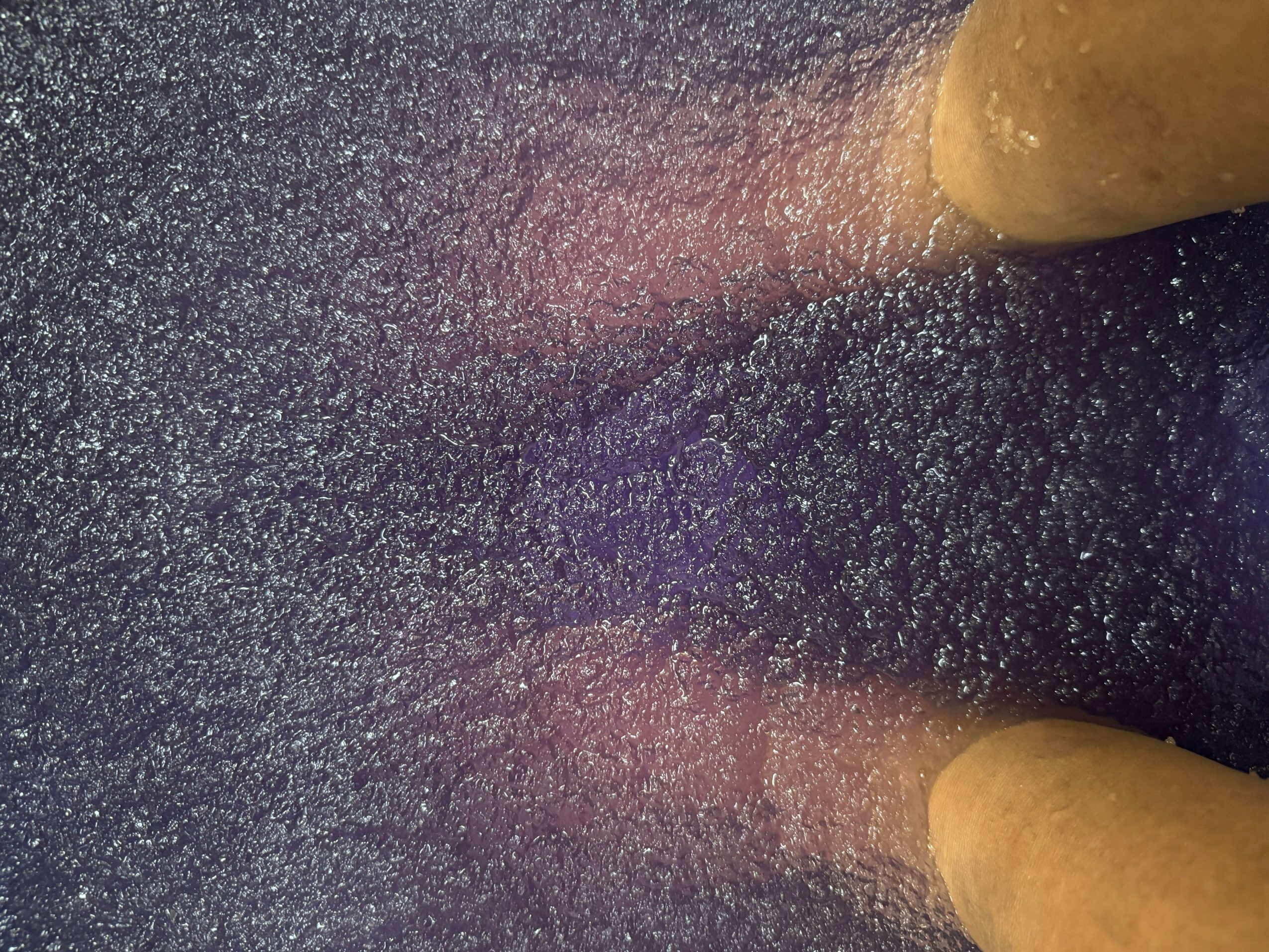 Close-up of a textured surface with two fingers visible at the top and bottom edges.