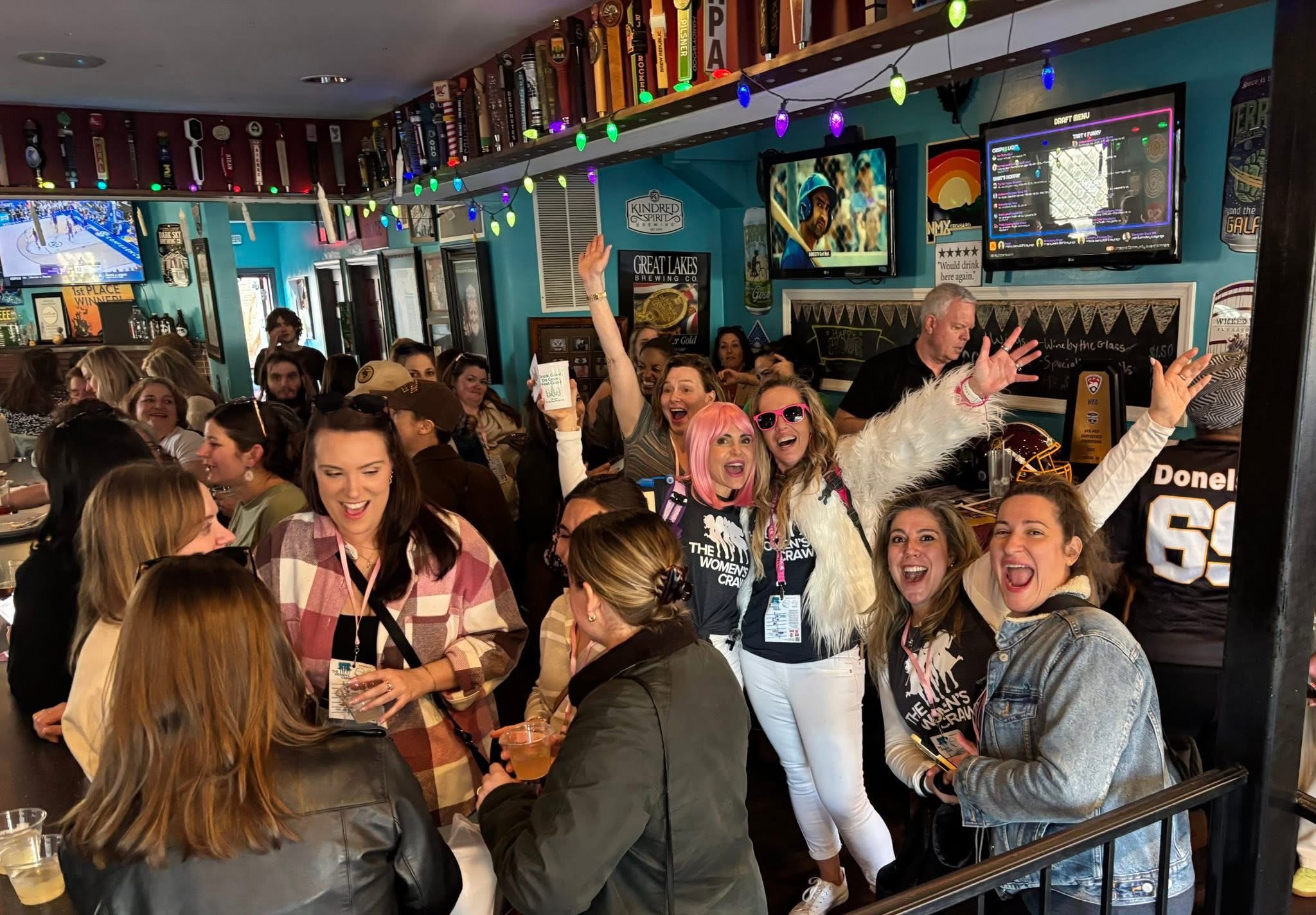 Group of people celebrating in a lively bar with colorful decorations and televisions on the wall.