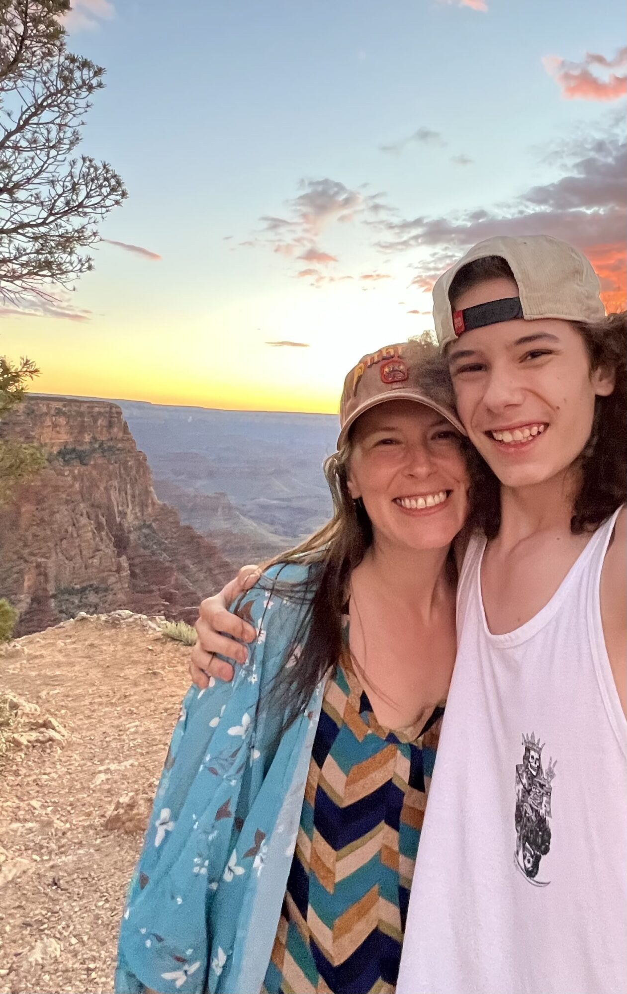 Two smiling women taking a selfie at the Grand Canyon during sunset, with cliffs and sky in background.