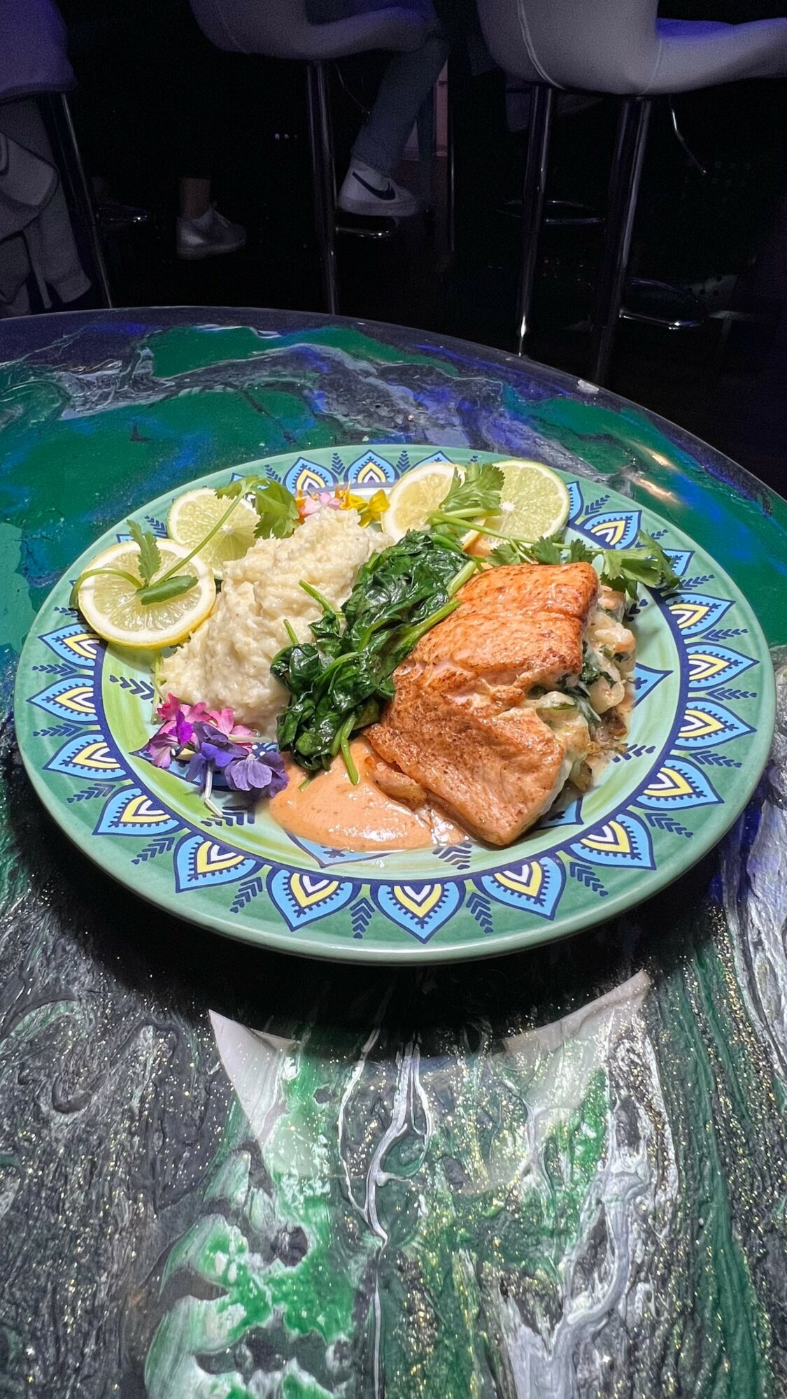 Plate with fried fish, rice, lime slices, and greens on a colorful patterned plate.