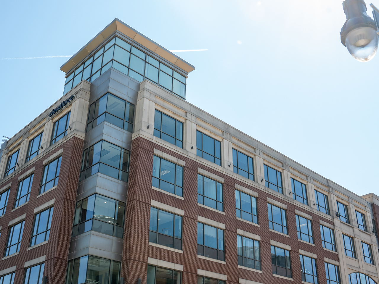 Modern multi-story building with glass windows and brick facade, under a clear sky with sunlight.