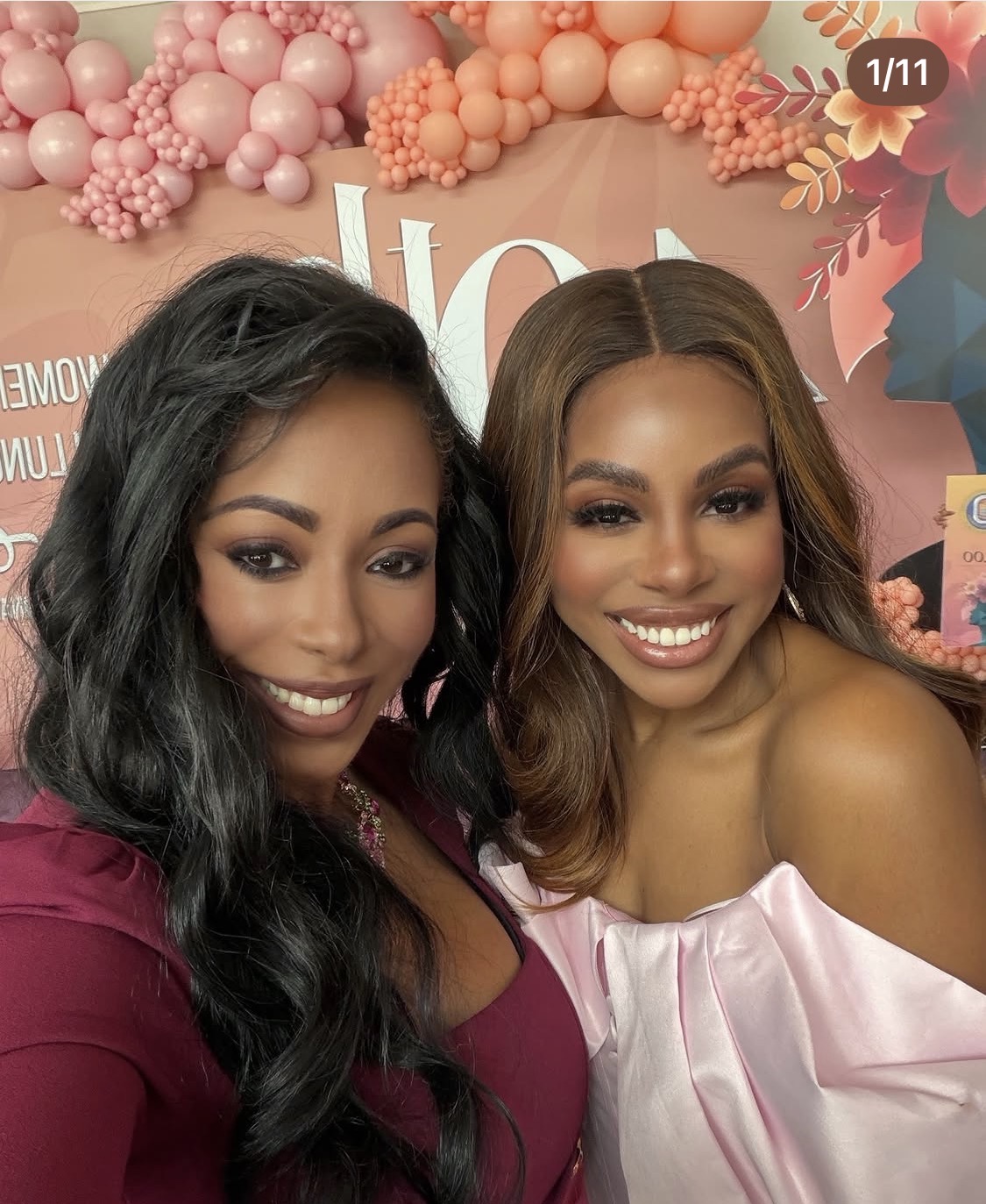 Two women smiling, one with long black hair and the other with shoulder-length brown hair, in front of a pink and floral background.