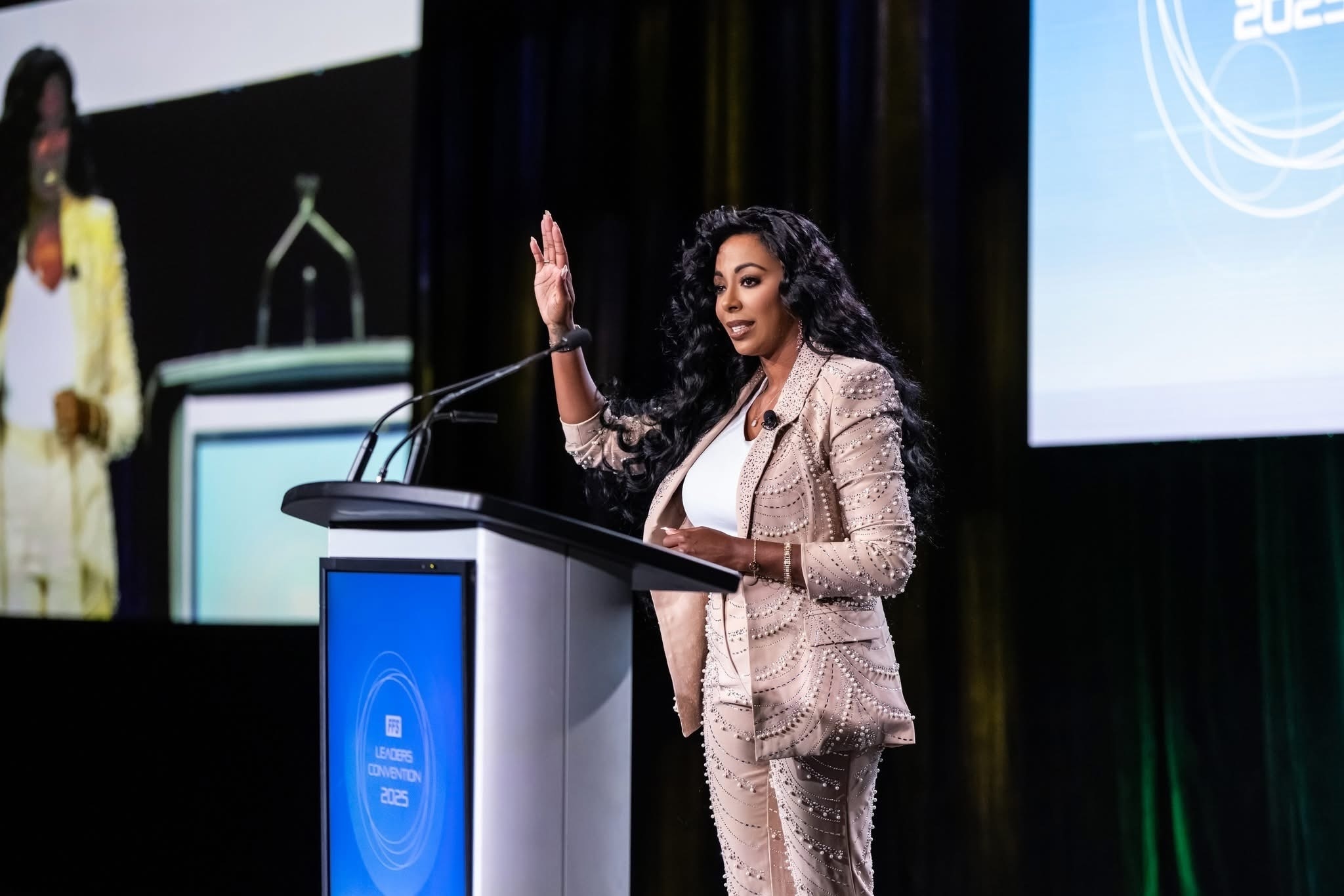 Woman with curly hair speaking at a podium during a conference or presentation.