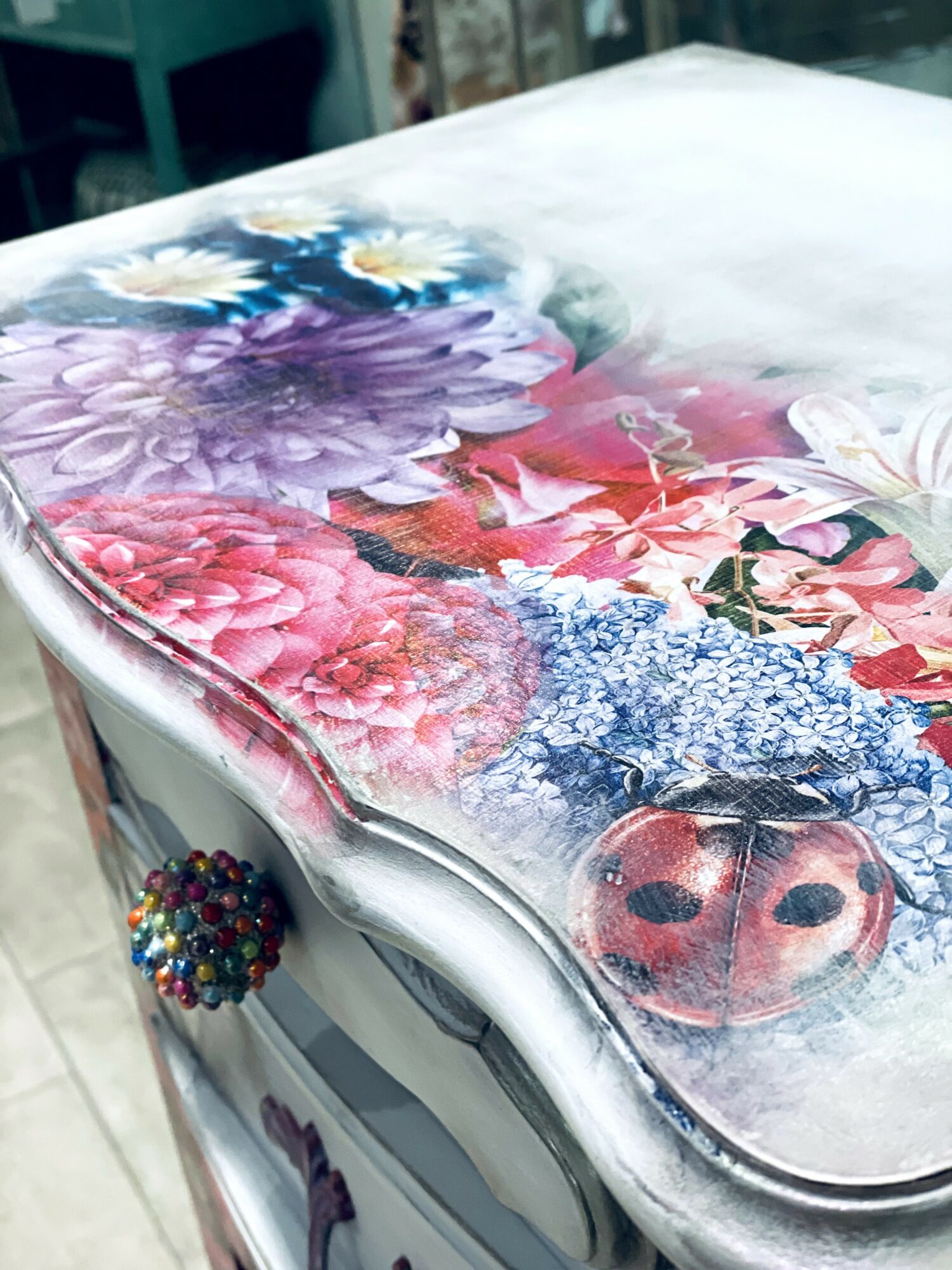 Decorative table with colorful floral and ladybug design, with a beaded handle on the side.